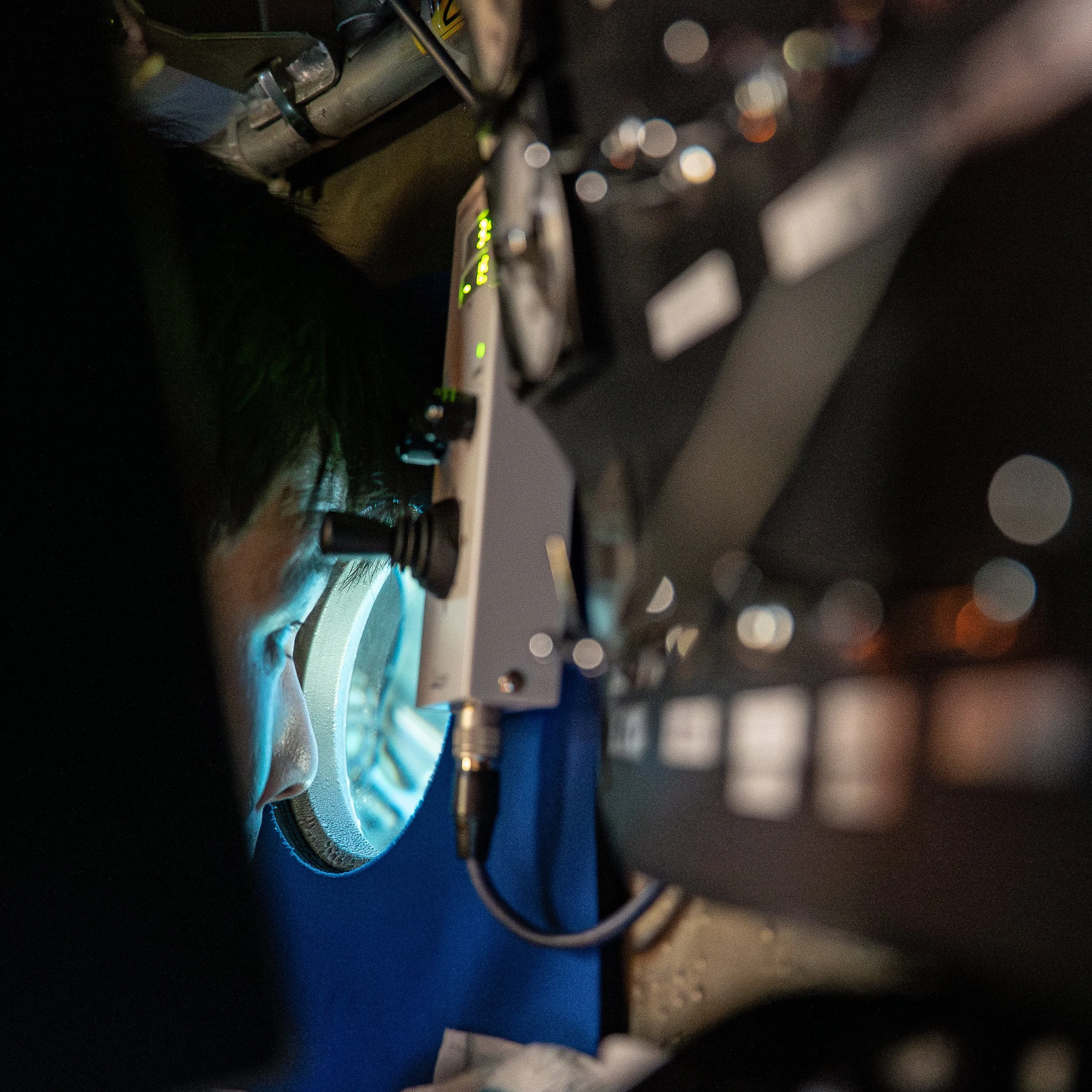 A scientist looks through a microscope in a lab setting with various equipment around.