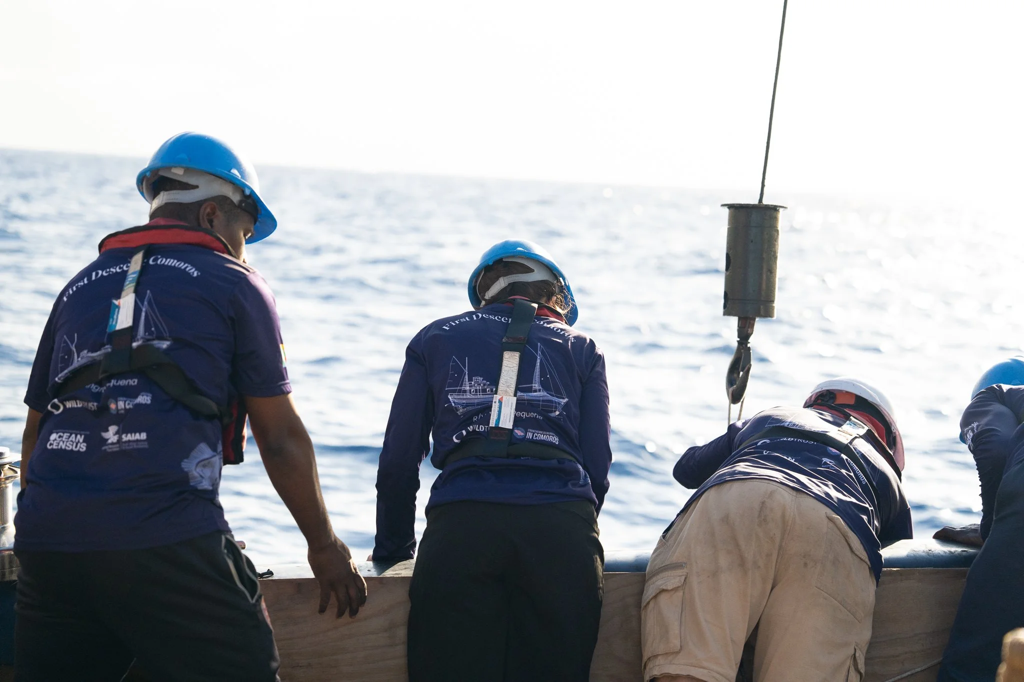 Seafarers working on a boat at sea, wearing safety gear and protective helmets.