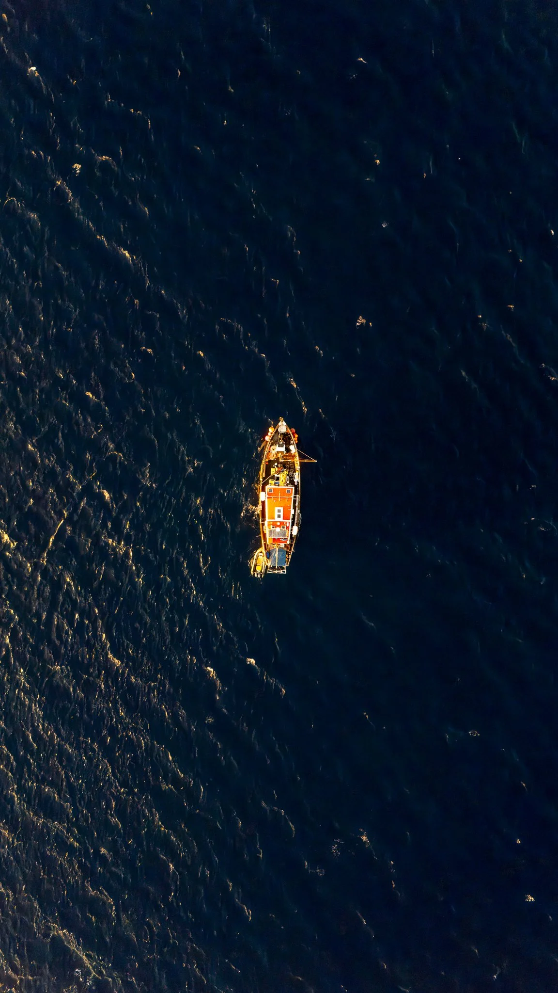 Aerial view of a boat on the ocean at sunset or sunrise.