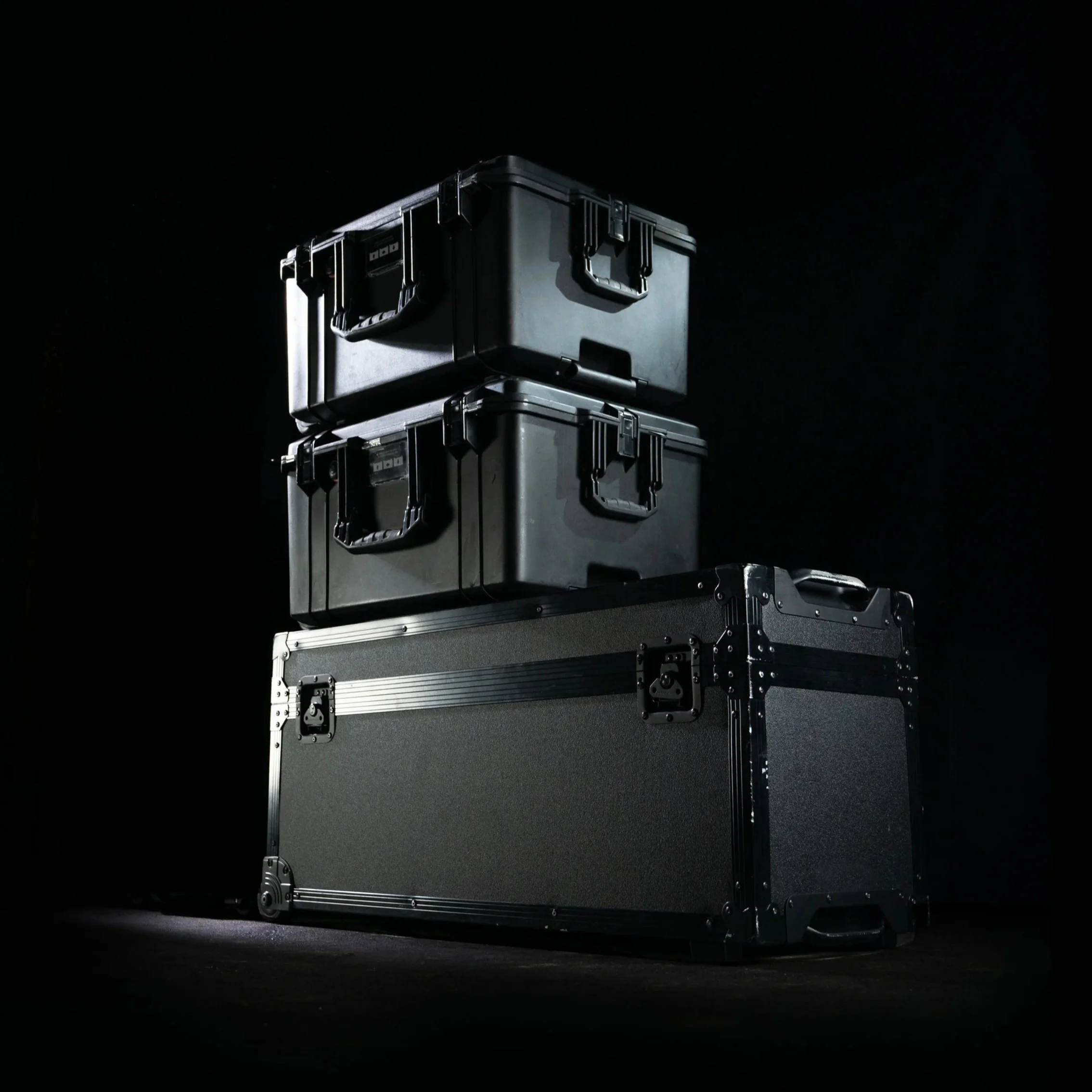 Three black protective cases stacked on top of a larger black storage case against a black background.