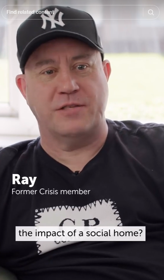 A man wearing a black cap with a white New York Yankees logo and a black T-shirt with a visible logo sitting indoors near a window. The text overlay indicates his name as Ray, a former Crisis member, and a subtitle reads 'the impact of a social home?'.