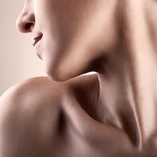 Close-up of a woman's face and shoulder, showing her smiling expression and smooth skin.
