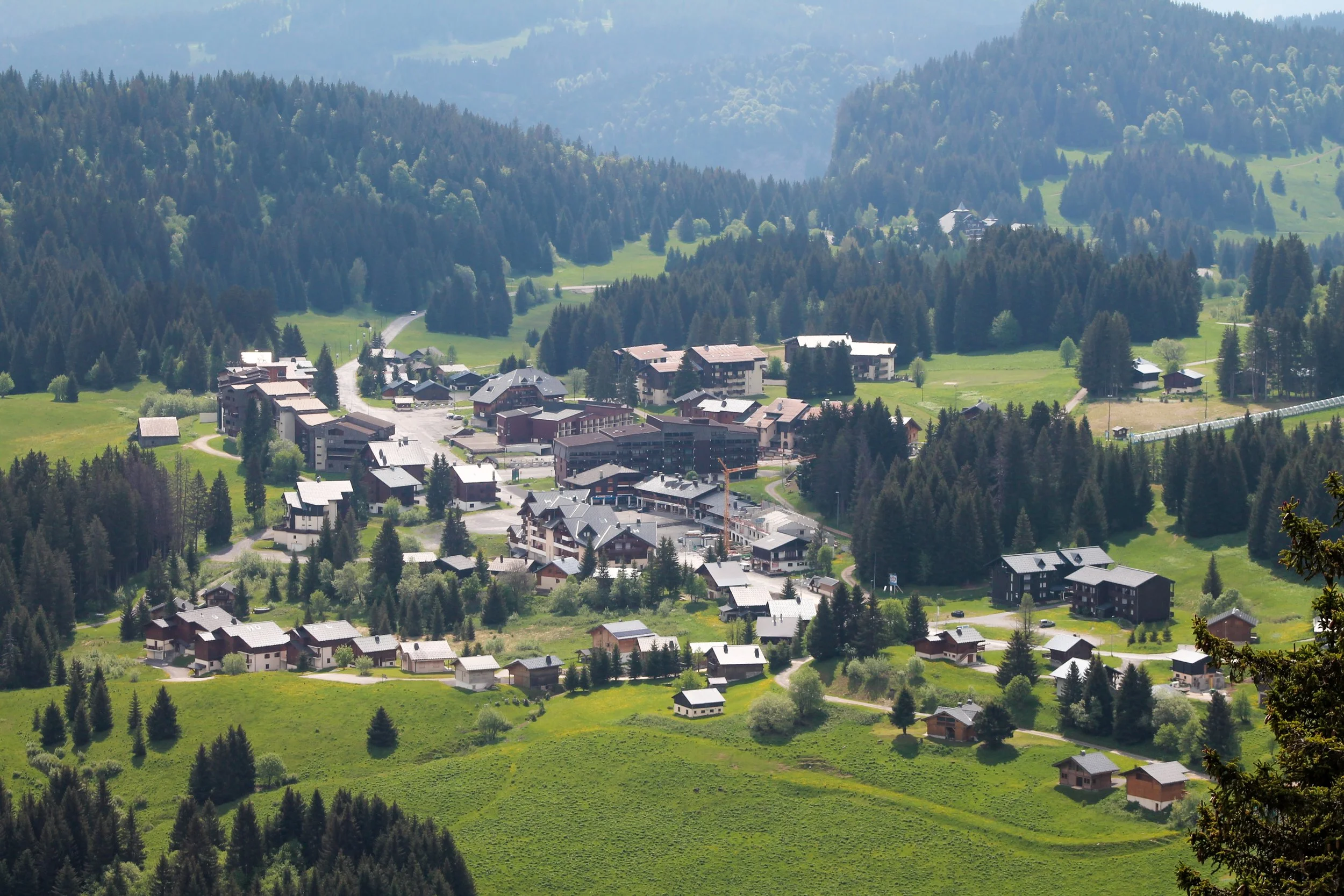 Petit village alpin avec des maisons en bois, entouré de forêts verdoyantes et de montagnes en arrière-plan