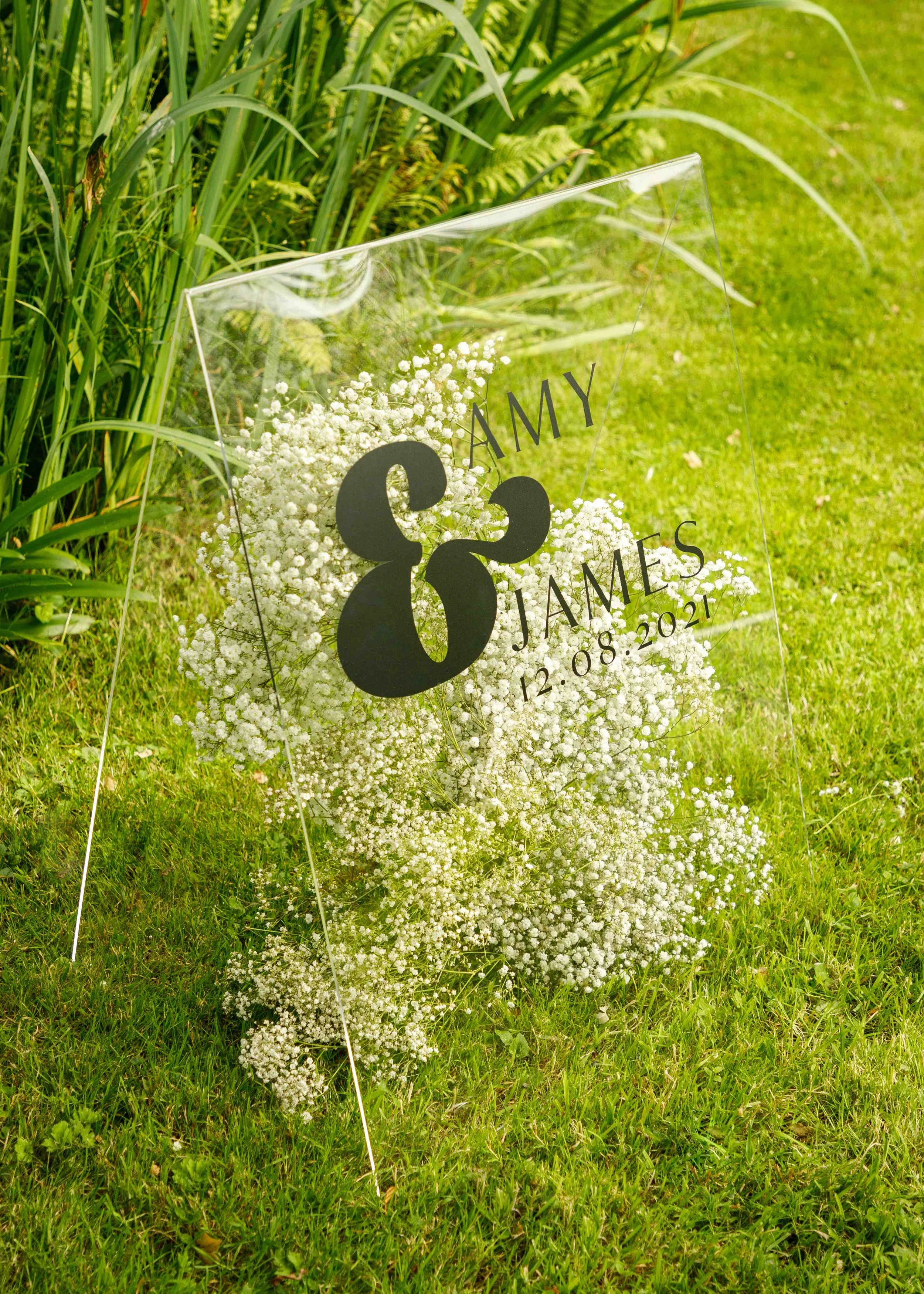 Modern acrylic wedding welcome sign with minimalist typography, styled amongst seasonal florals for an outdoor wedding celebration.