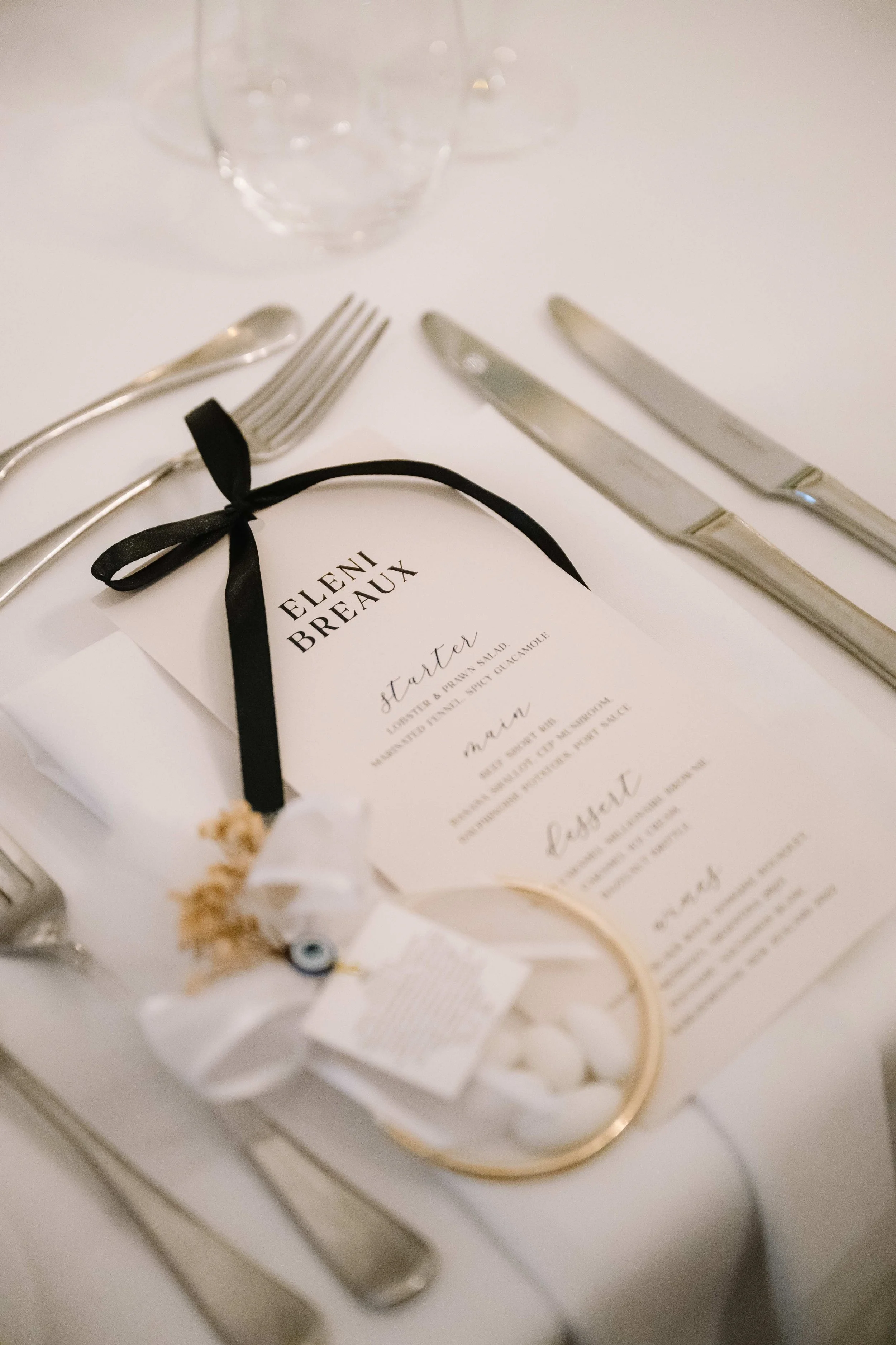 Wedding place setting with a program, silverware, and glasses on a white tablecloth.