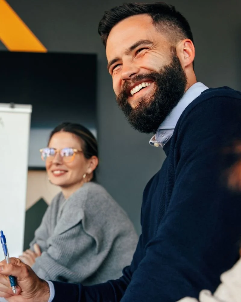Seren Delta DIgital Transformation Services - Intelligent Architecture. A man with a beard and a woman with glasses sitting at a table, both smiling and appearing to enjoy a discussion or meeting in a professional setting.
