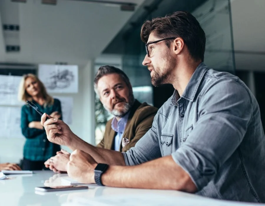 Seren Delta DIgital Transformation Services - Enterprise Architecture Services. Three people engaged in a discussion in a modern office, with one person speaking, two listening, and a woman in the background.