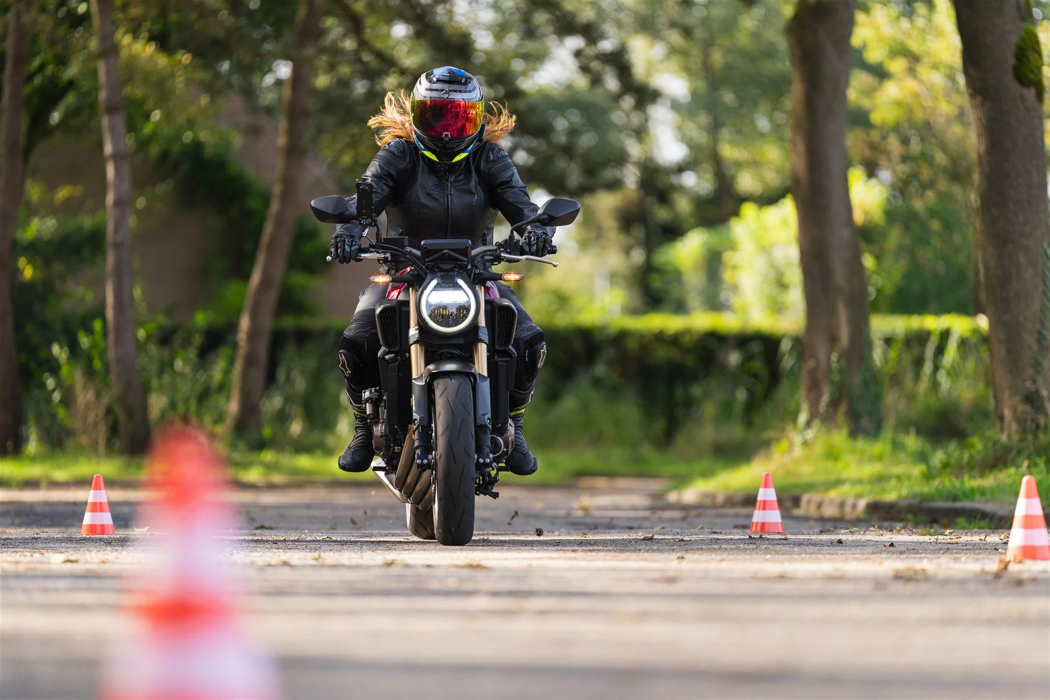 Woman riding with wind in het hair on motorcycle, Honda CB650R with E-Clutch in between cones