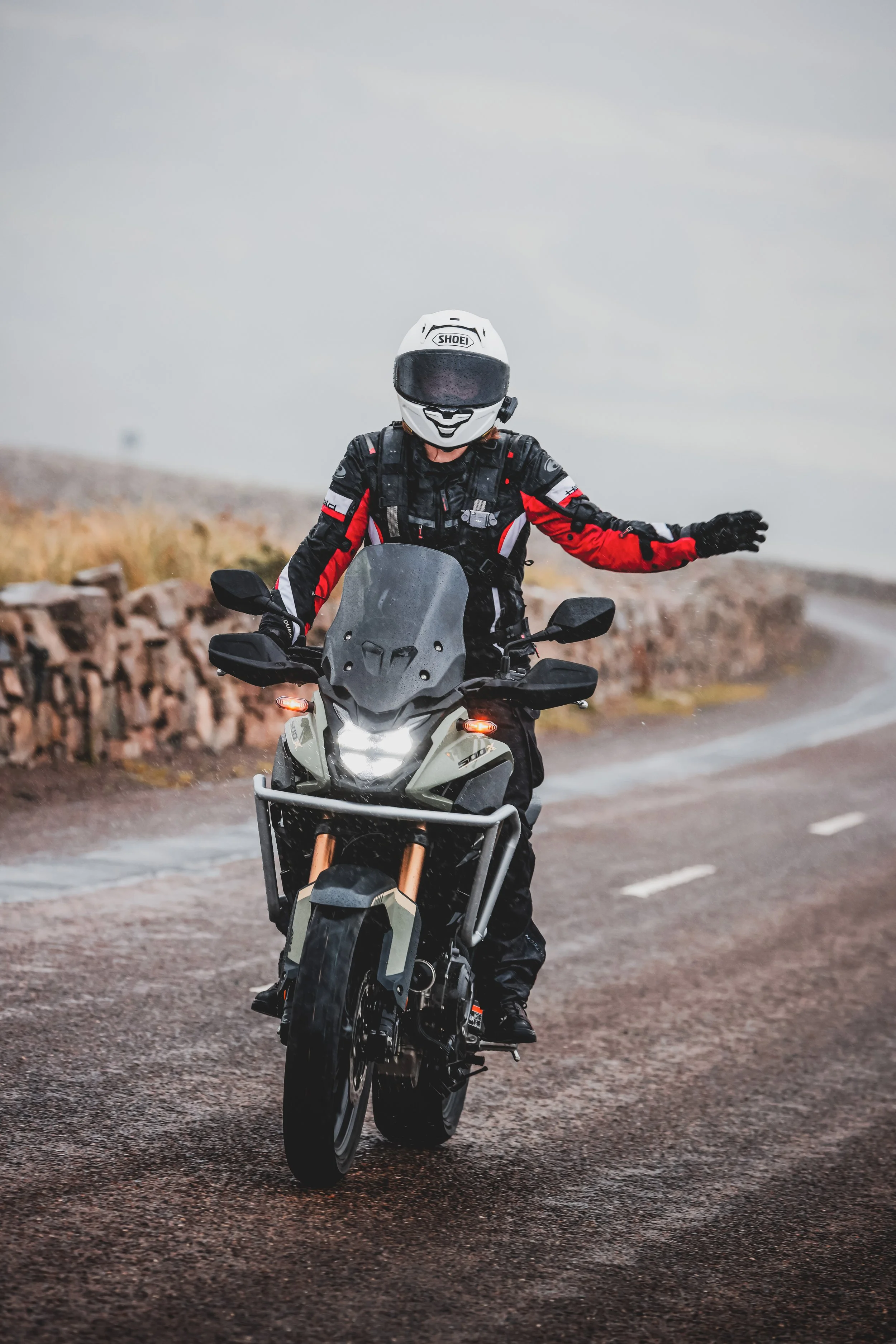 A motorcycle rider wearing a white helmet and black and red gear riding on a wet road in foggy weather.