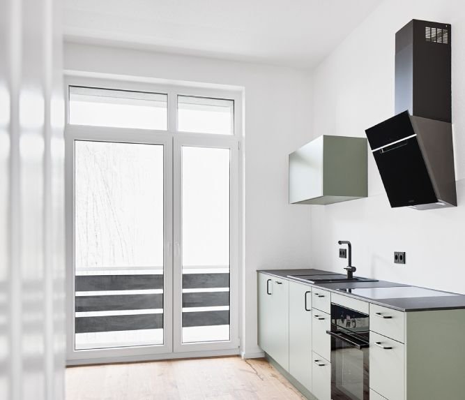Küche mit weißen Schränken, schwarzem Herd, Dunstabzugshaube und einer großen Fenster-Glastür.