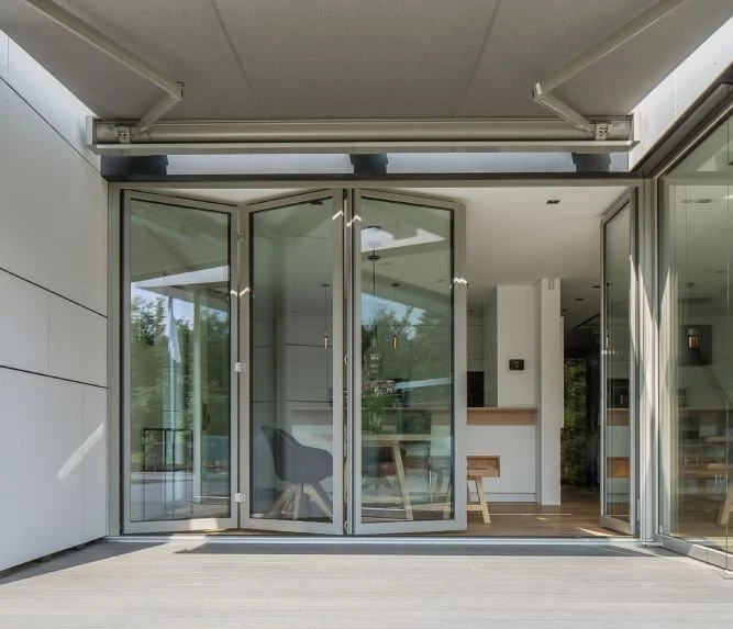 Moderne Villa mit großer Glas-Falttürenanblage, die zum Garten führen, mit Blick ins Innere, inklusive minimalistischem Interieur.