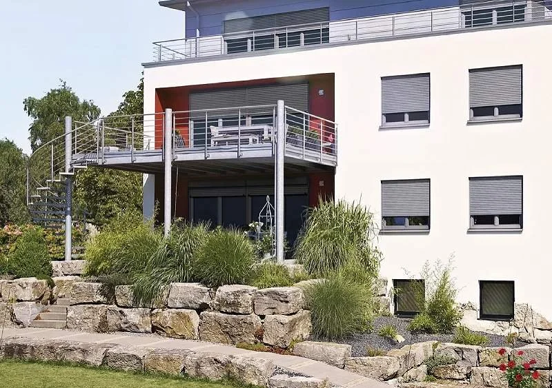 Modernes weißes Wohngebäude mit Balkon, Garten und Schachtrollläden.