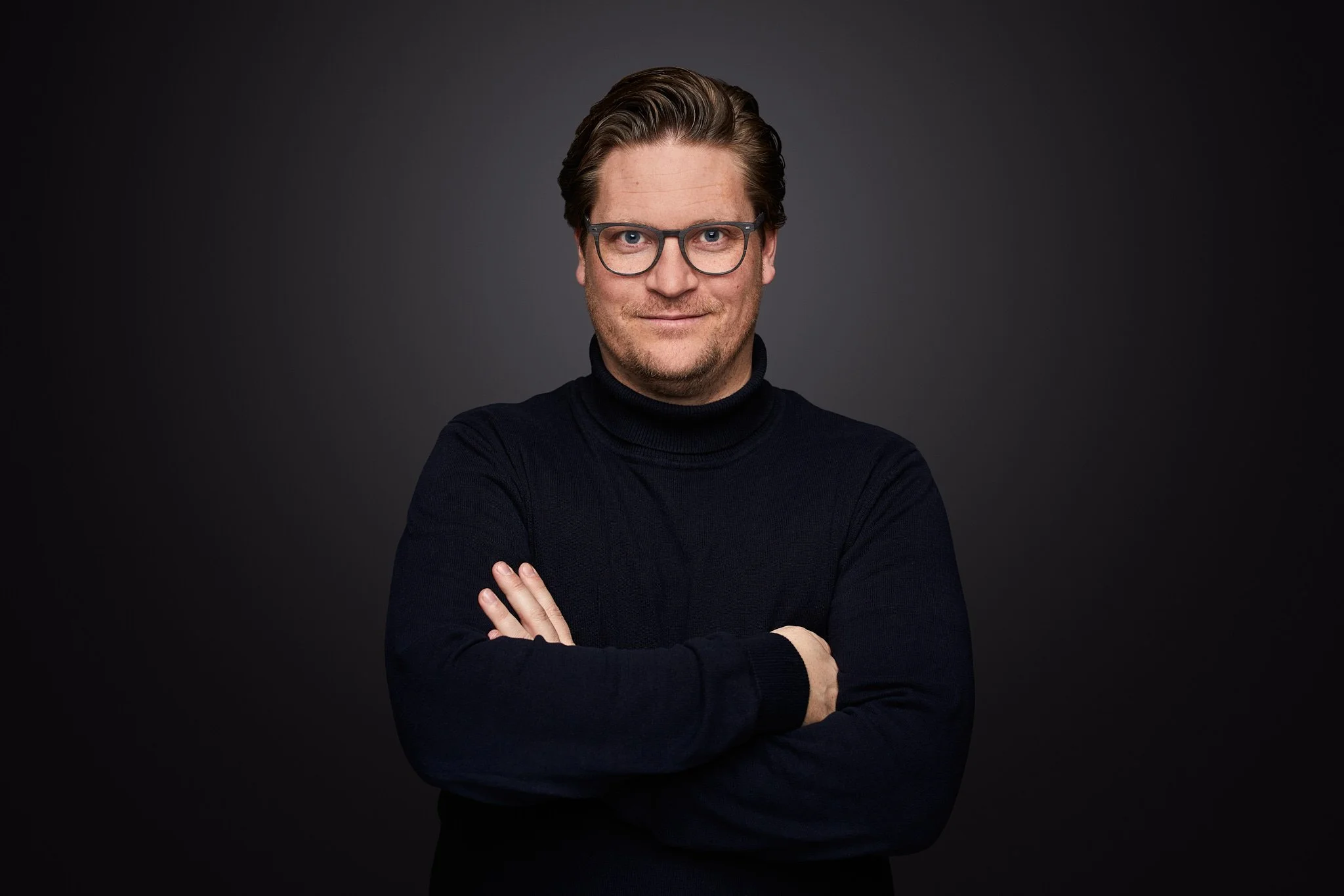 Fischbach Fenster Gründer und Geschäftsführer Michael Fischbach, Brille und dunklem T-Shirt steht vor einem dunklen Hintergrund, die Arme verschränkt.
