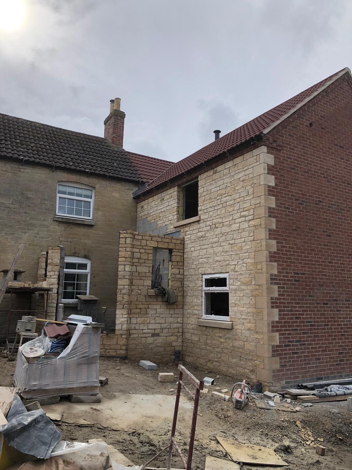 Construction site of a house with walls partially built with beige bricks and some areas covered with red bricks, on a cloudy day.