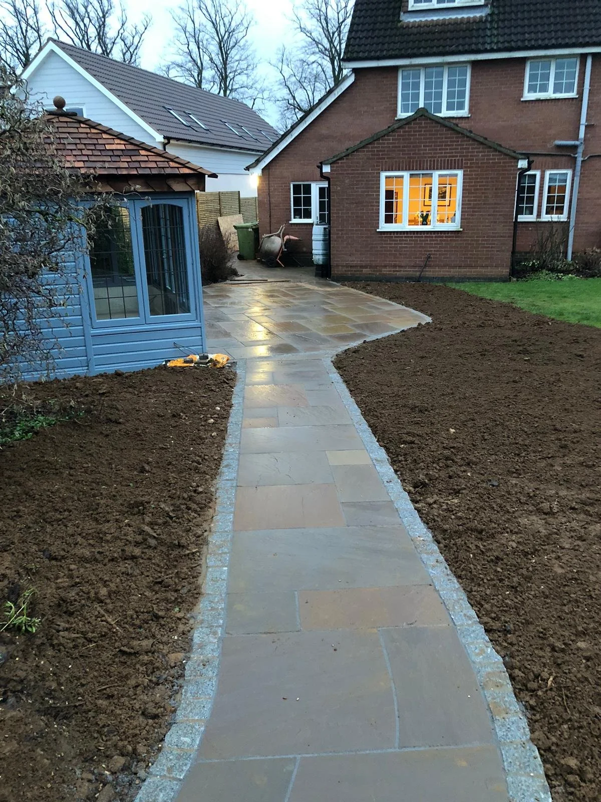 A newly paved stone pathway leading to the back of a house, flanked by soil beds on each side completed by local Grantham builder G East Builder.