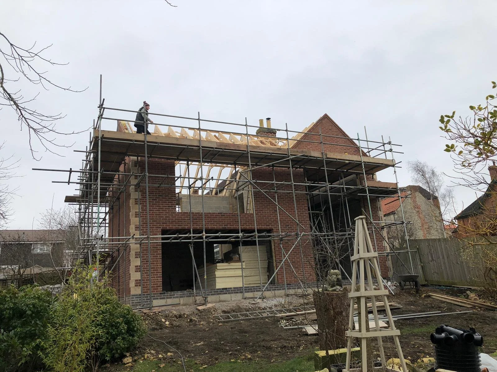 A house under construction with scaffolding around it, workers on the roof framing completed by local Grantham builder G East Builder.