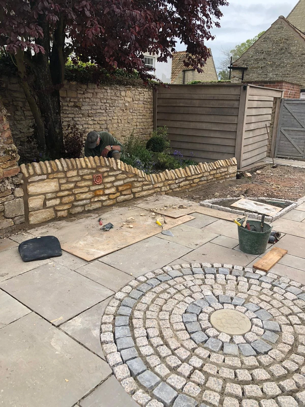 Grantham builder G East Builder. working on building a small brick wall in a garden, with construction tools and materials scattered around.