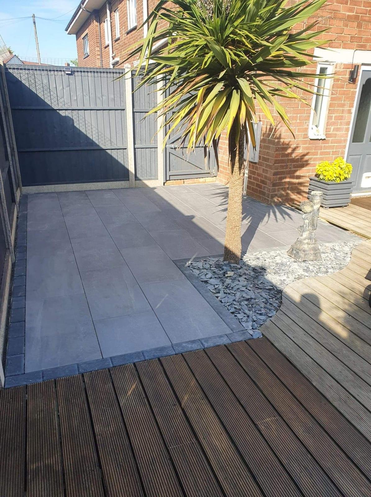 A backyard patio area with a large potted plant, a small sculpture, a flower pot, and a wooden deck completed by local Grantham builder G East Builder.