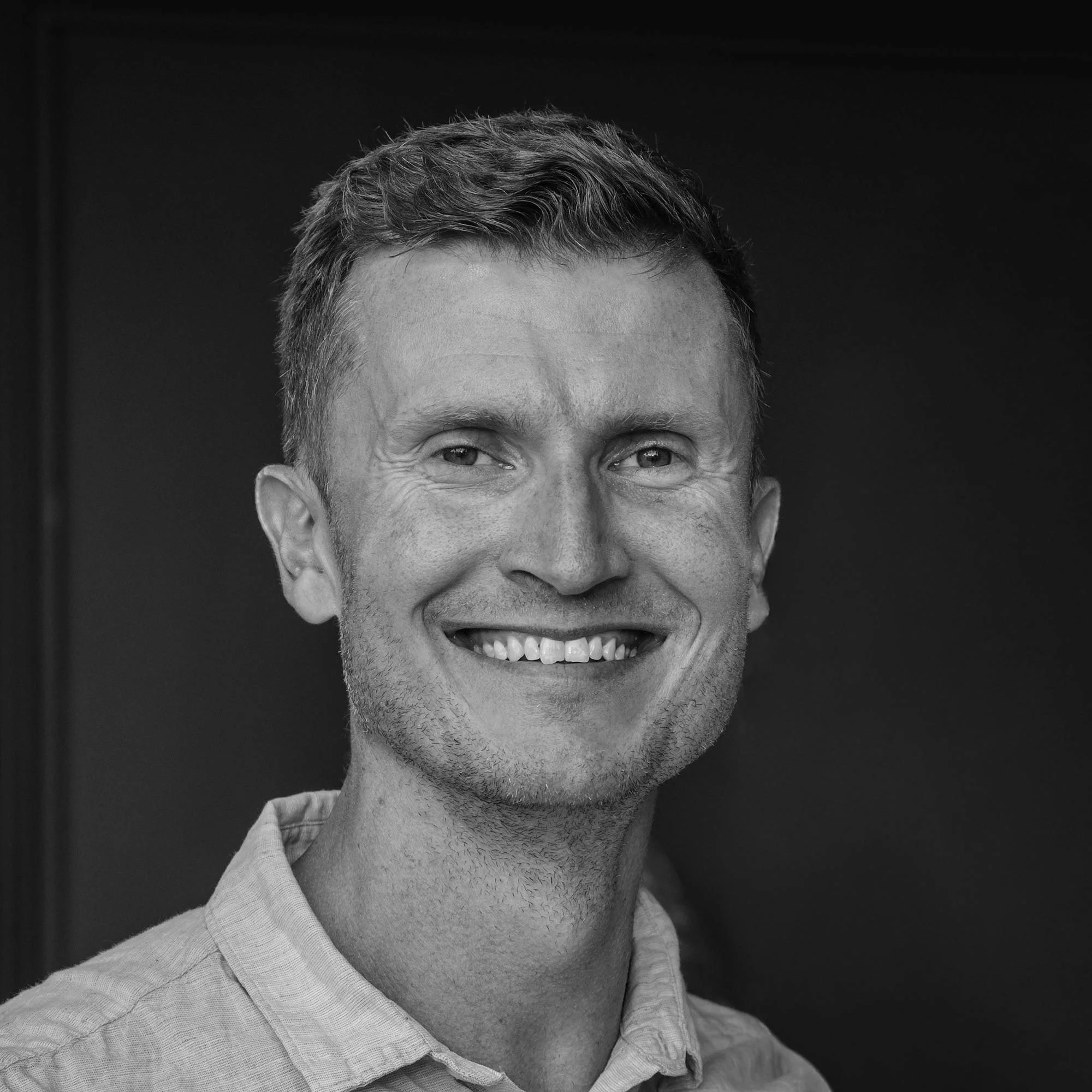 Black and white photo of a smiling man with short, wavy hair wearing a collared shirt.