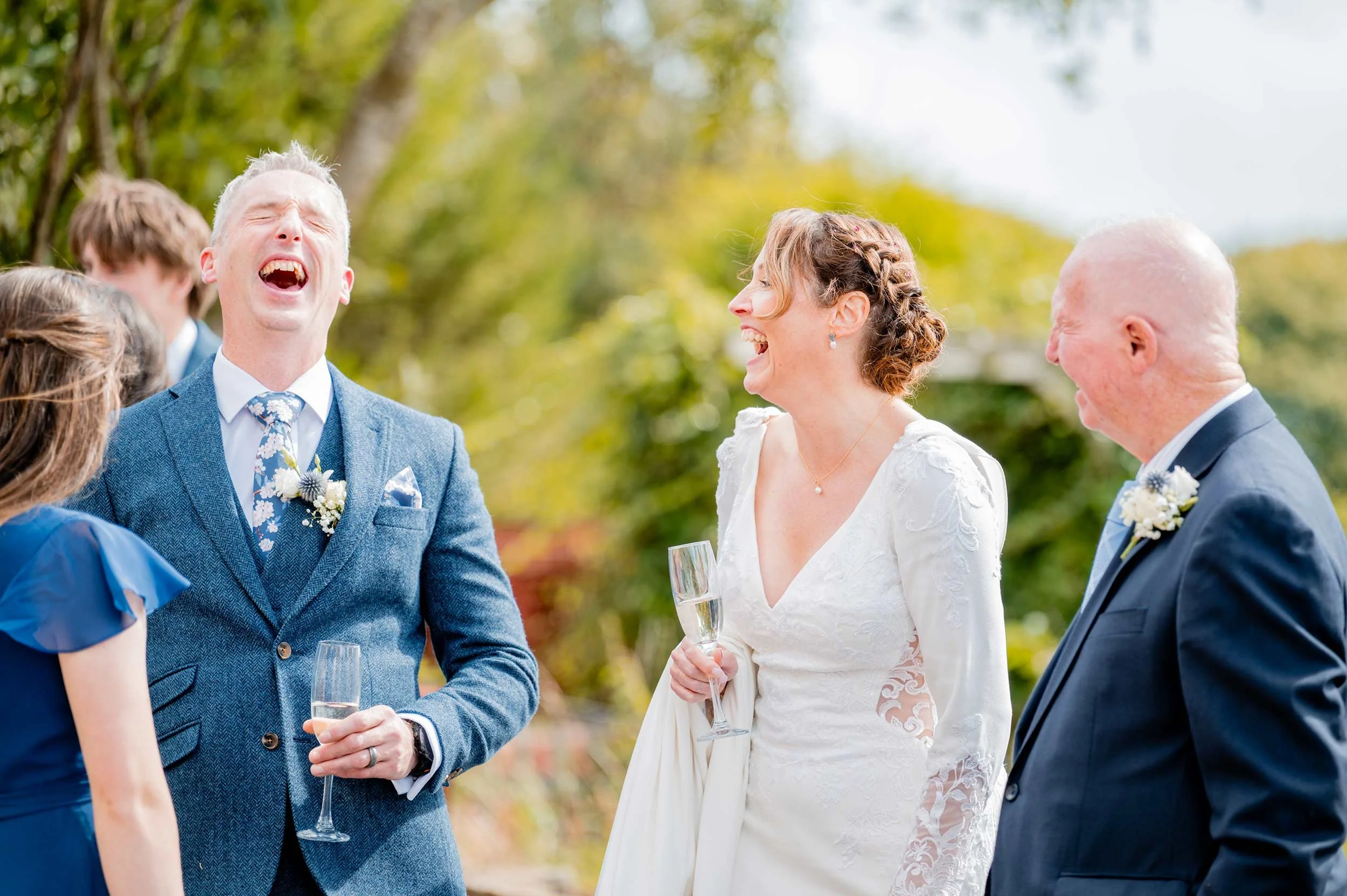 People celebrating at an outdoor wedding, smiling and laughing, holding champagne glasses.