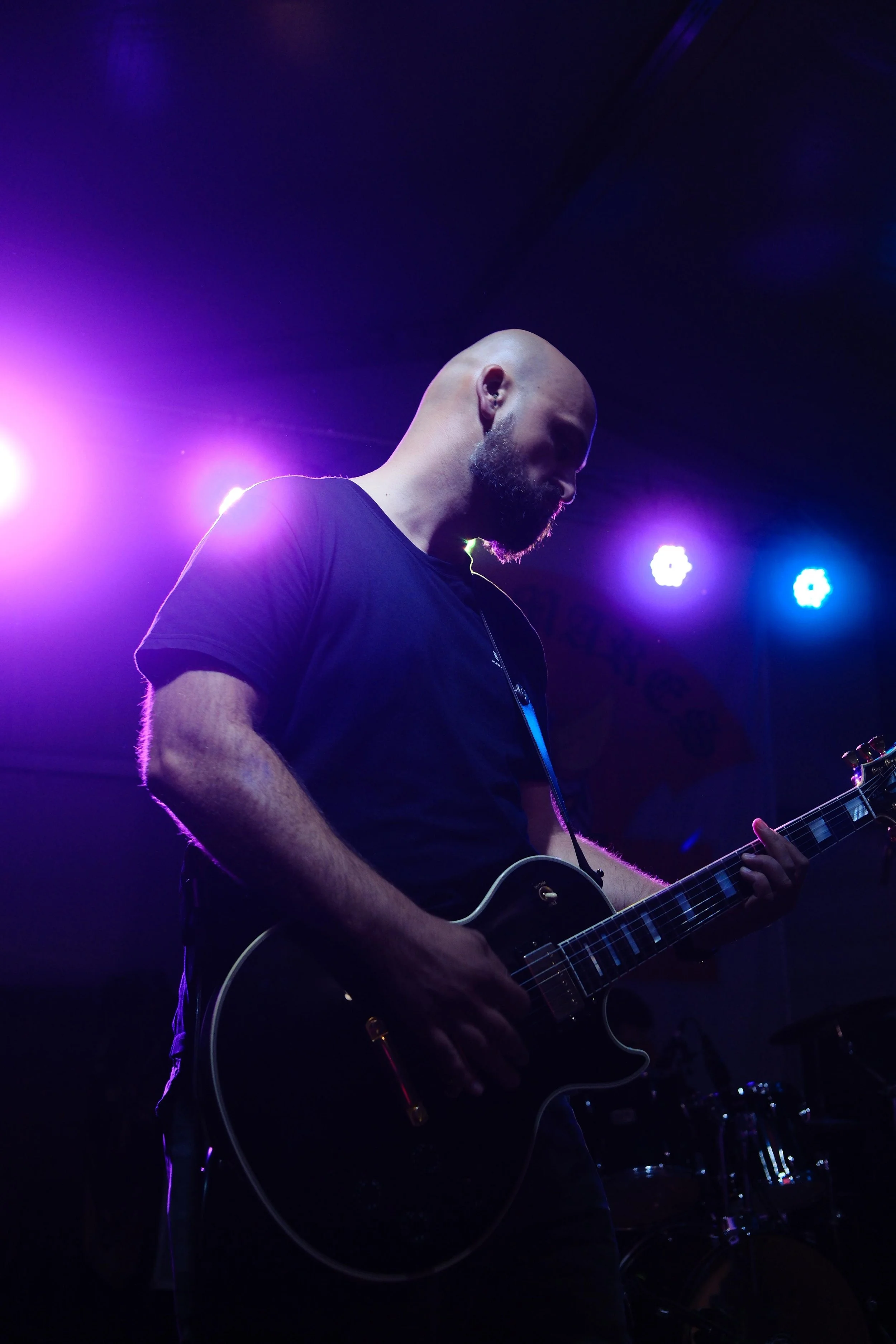A man plays an electric guitar on stage with purple and blue stage lighting.