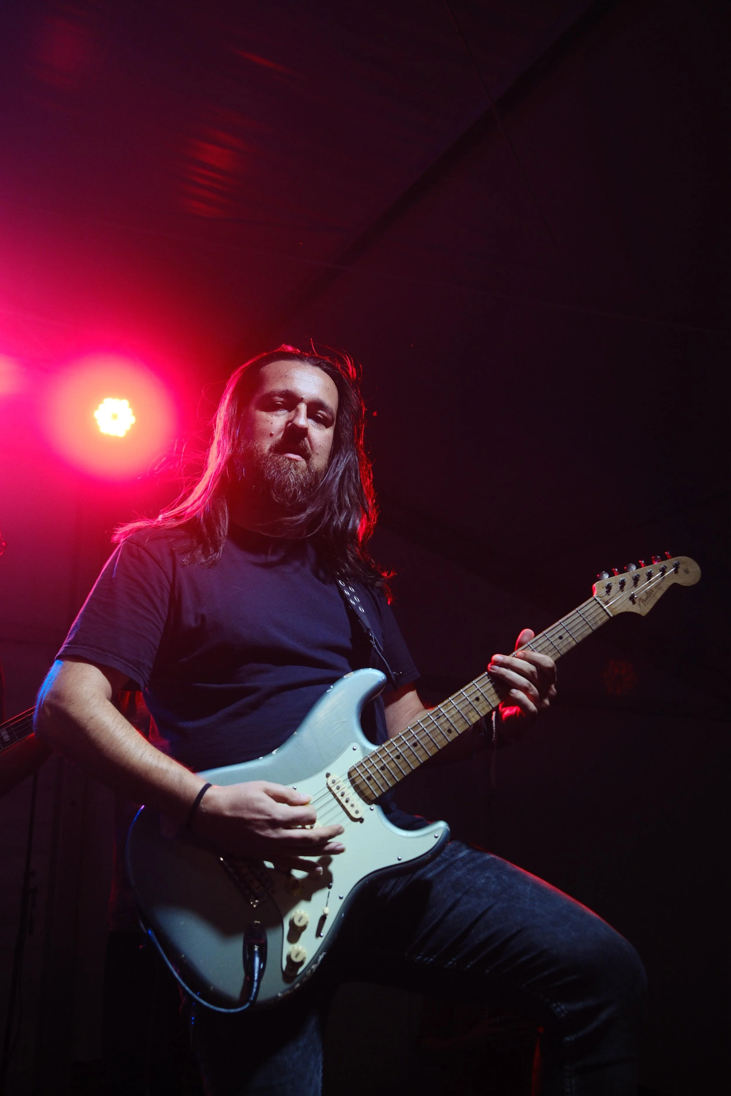 Guitarist performing on stage under red lights, playing an electric guitar.