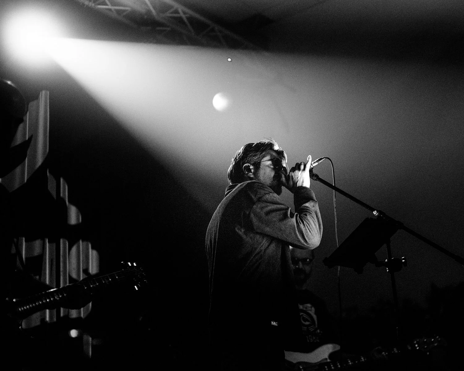 A man performing on stage at a concert, singing into a microphone with a spotlight illuminating him, in black and white.