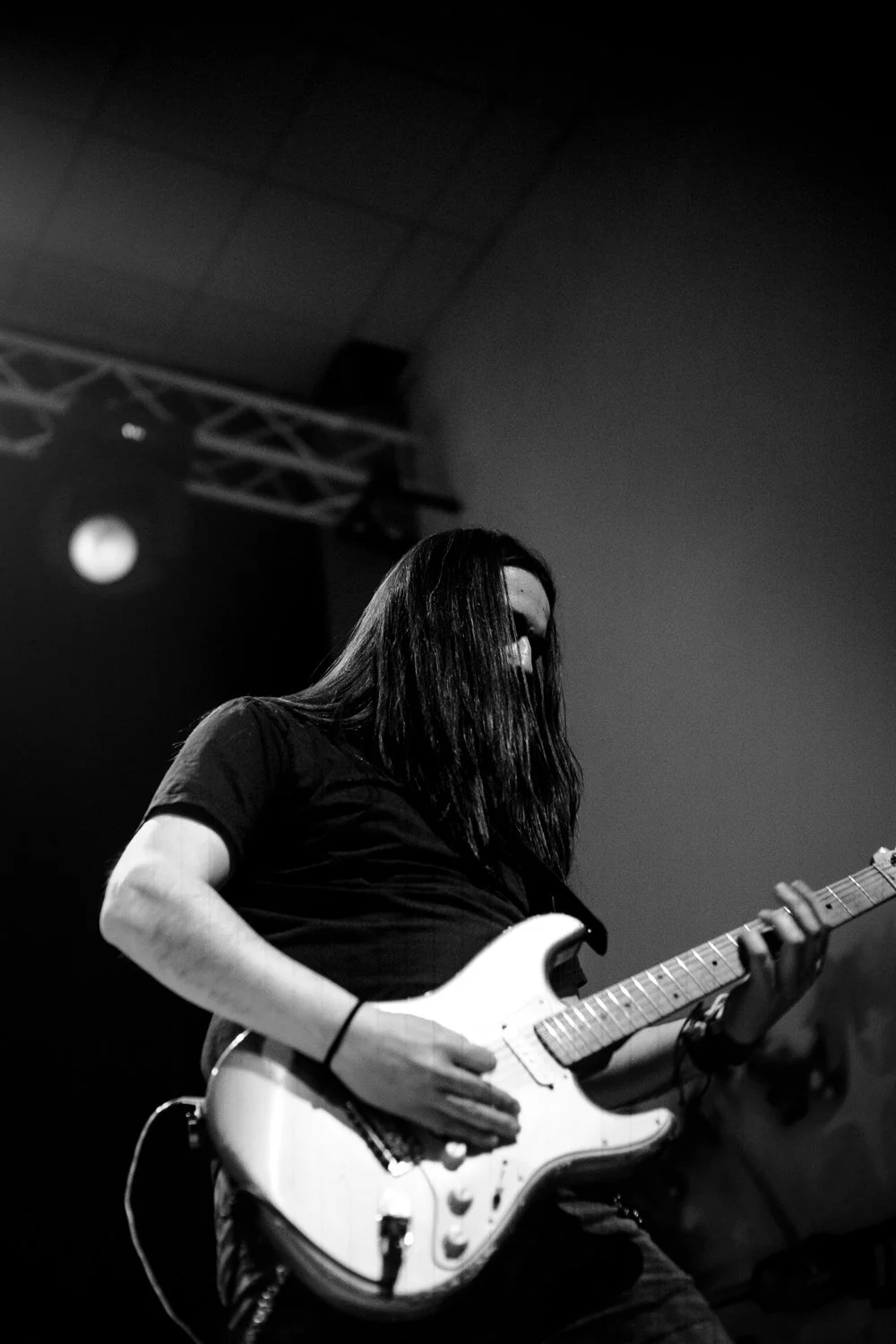 A person with long dark hair playing an electric guitar on stage at a concert, black and white photo.