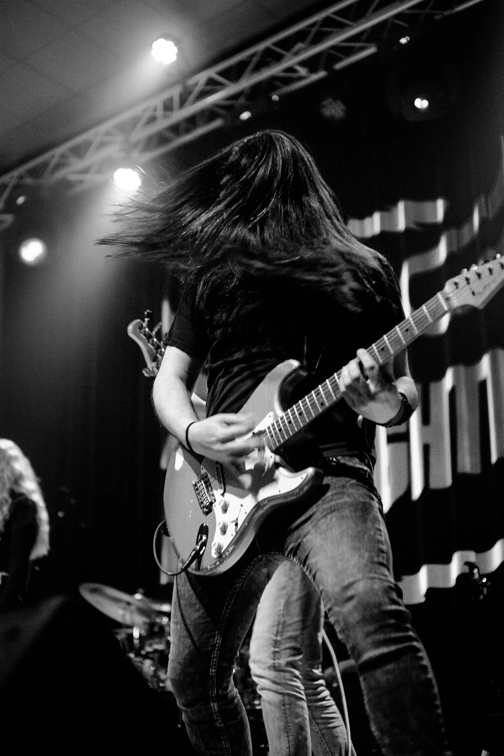 A person playing an electric guitar on stage with long hair, black and white photograph, stage lighting, and musical equipment.