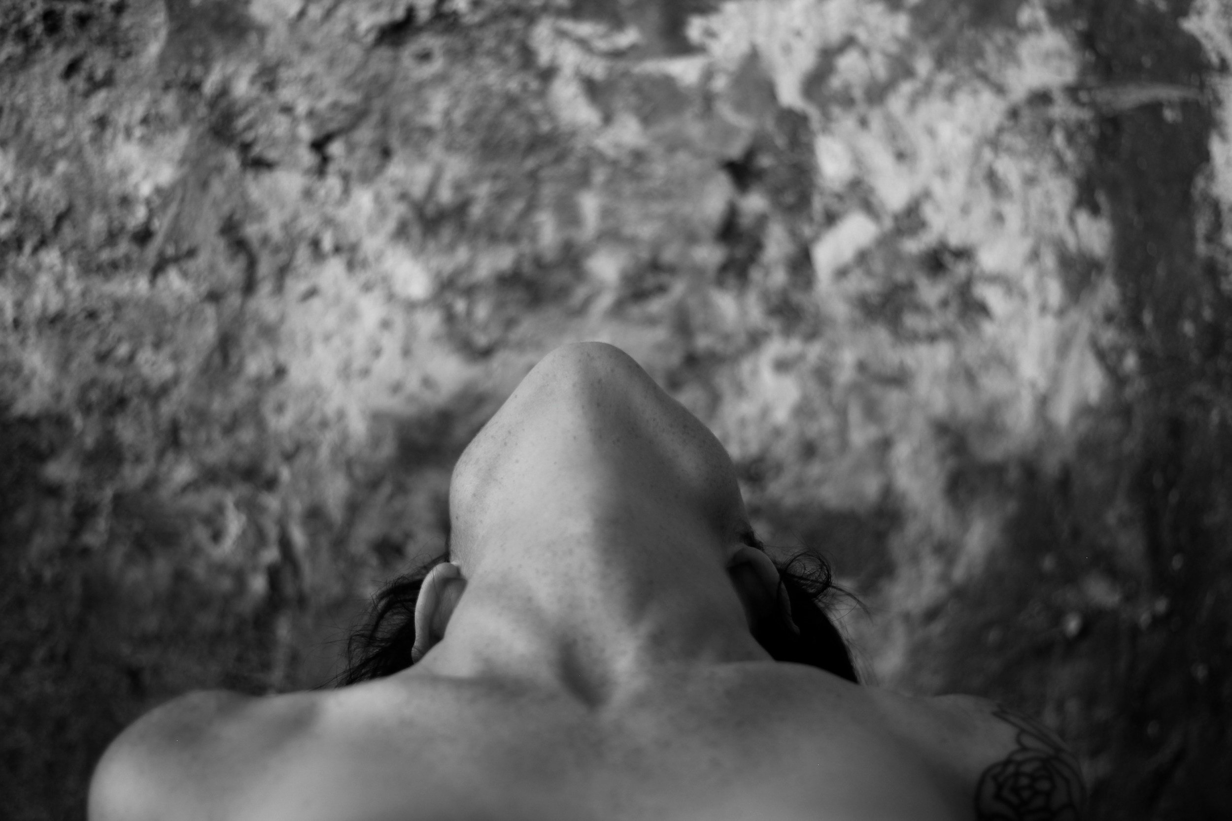 Top-down black and white photograph of a person's face with nose and forehead visible, lying on a rough surface.