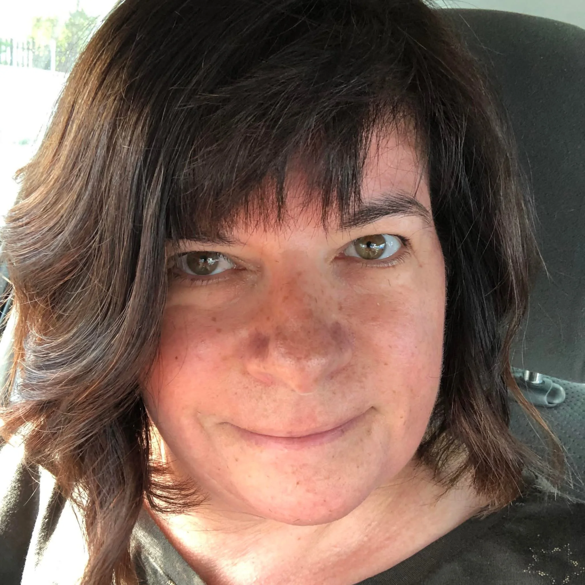 Close-up of a woman with brown wavy hair and hazel eyes, smiling softly.