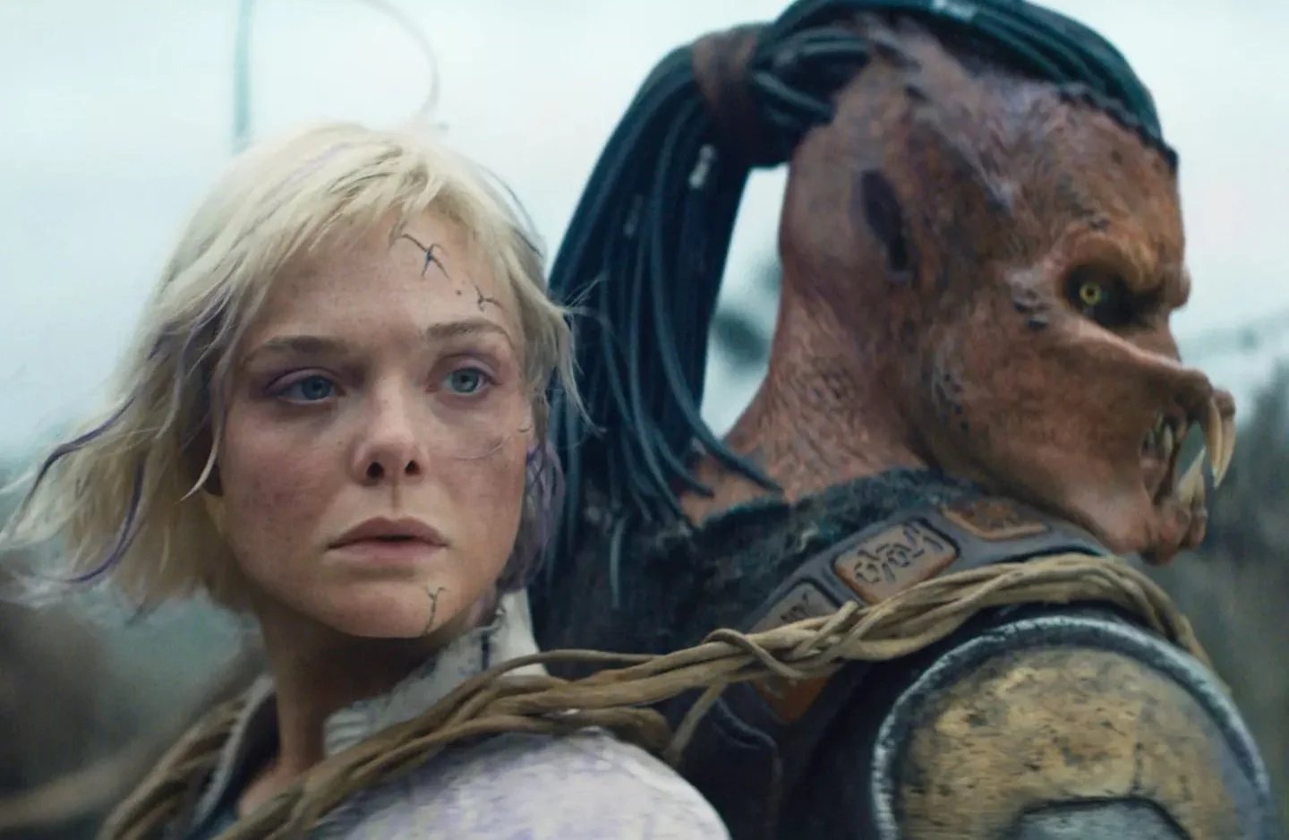 A woman with blonde hair and a scarred face standing next to a humanoid alien with reptilian features and dark hair.