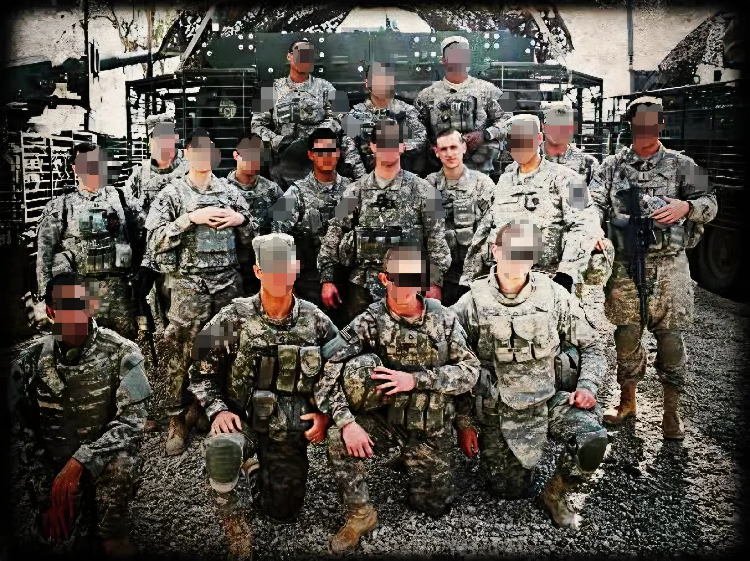 Group of soldiers in camouflage uniforms posing outdoors in front of military vehicles.