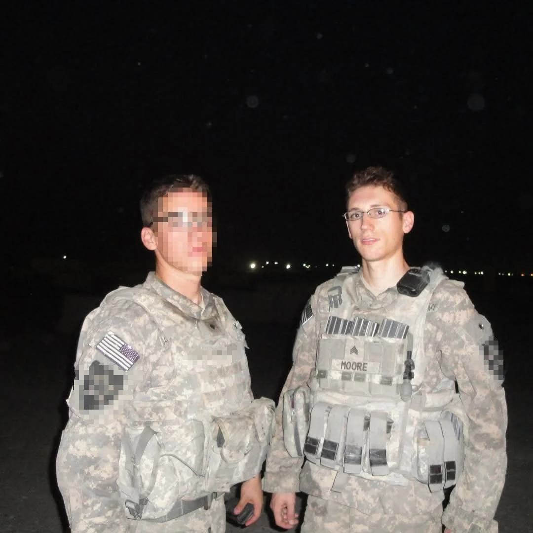 Two soldiers in camouflage uniforms shaking hands at night with city lights in the background.