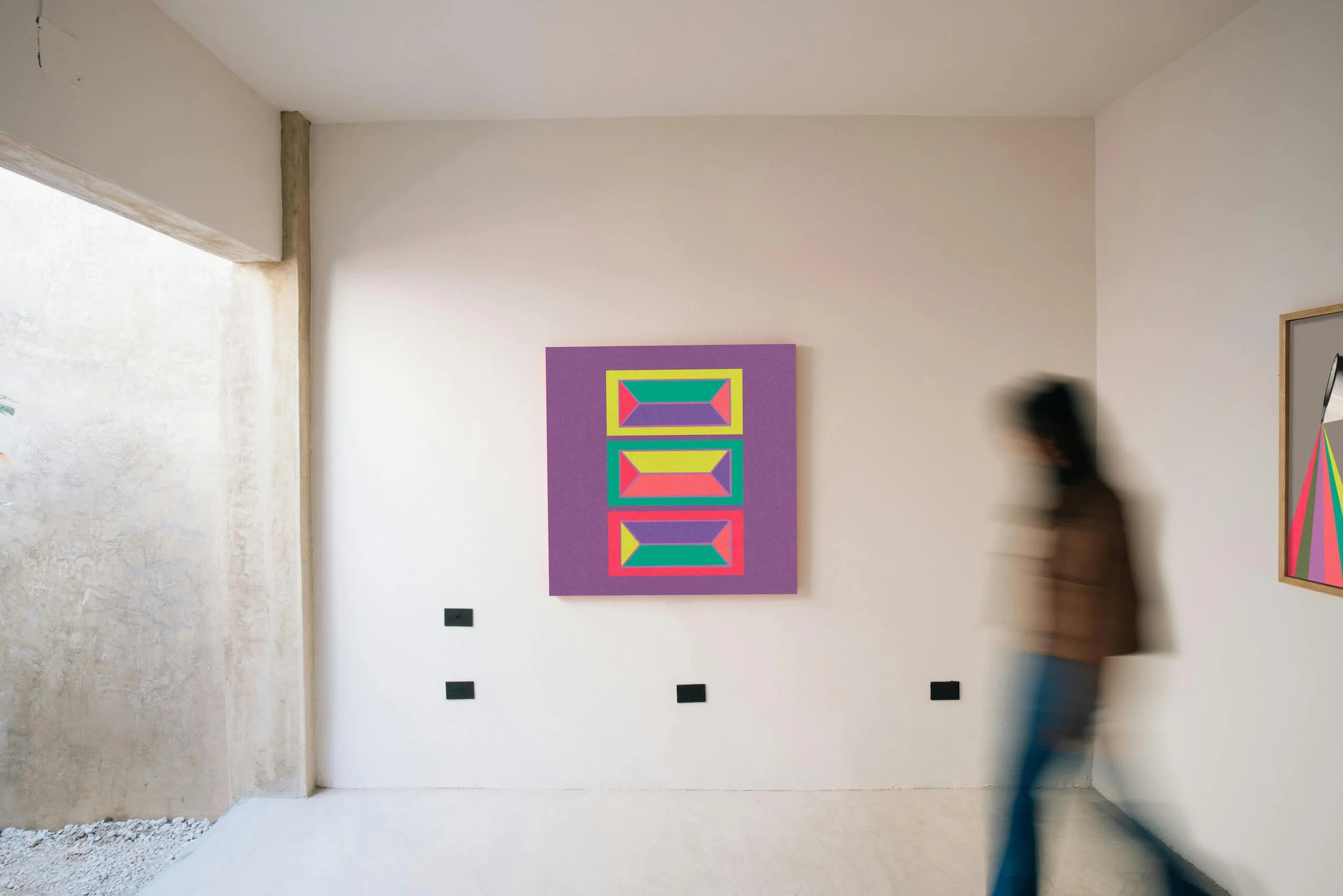 An art gallery with a colorful geometric painting on the wall and a person walking past, blurred due to motion.