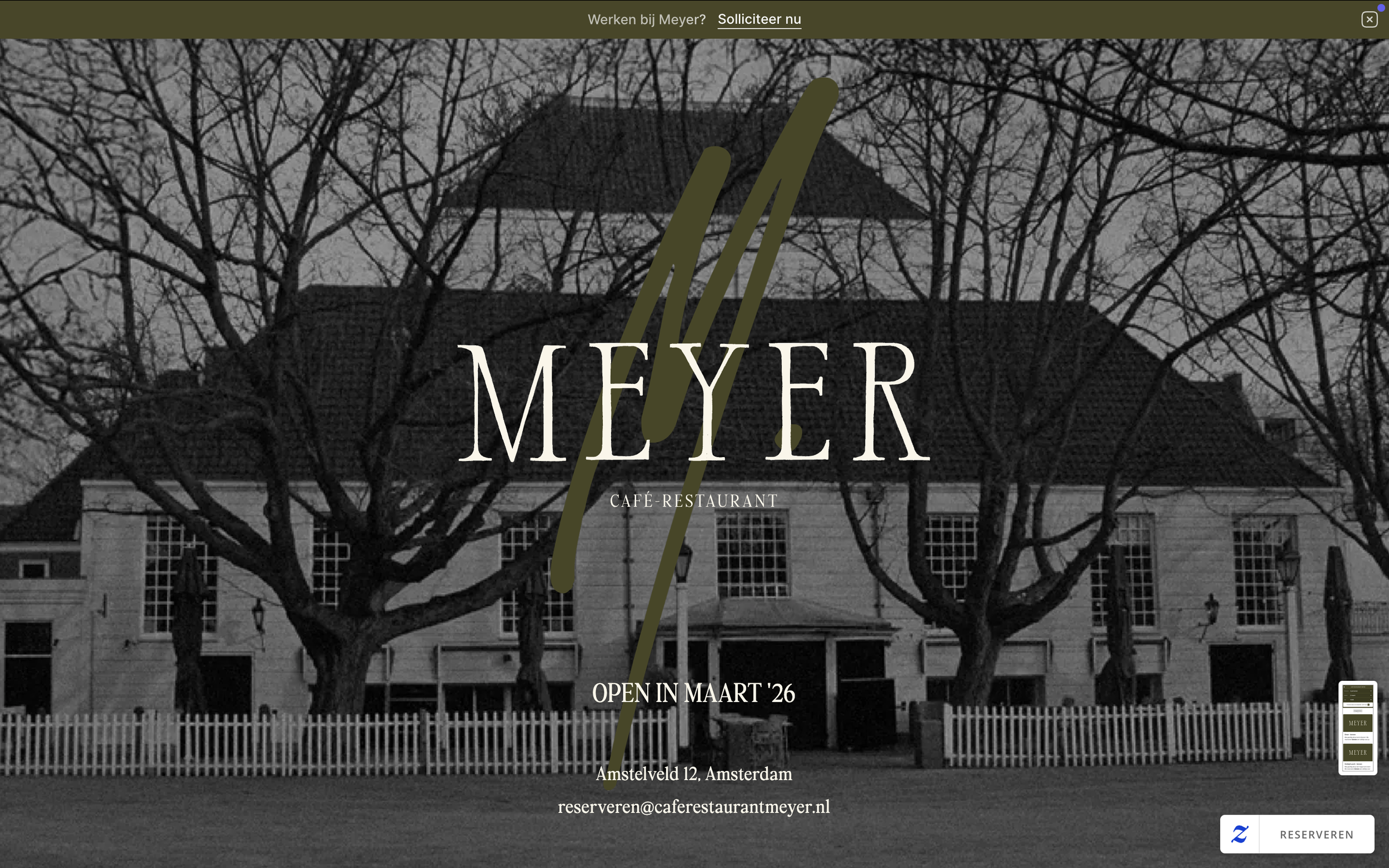 Black and white photo of a historic building with a peaked roof and multiple windows, surrounded by leafless trees and a white picket fence in front.