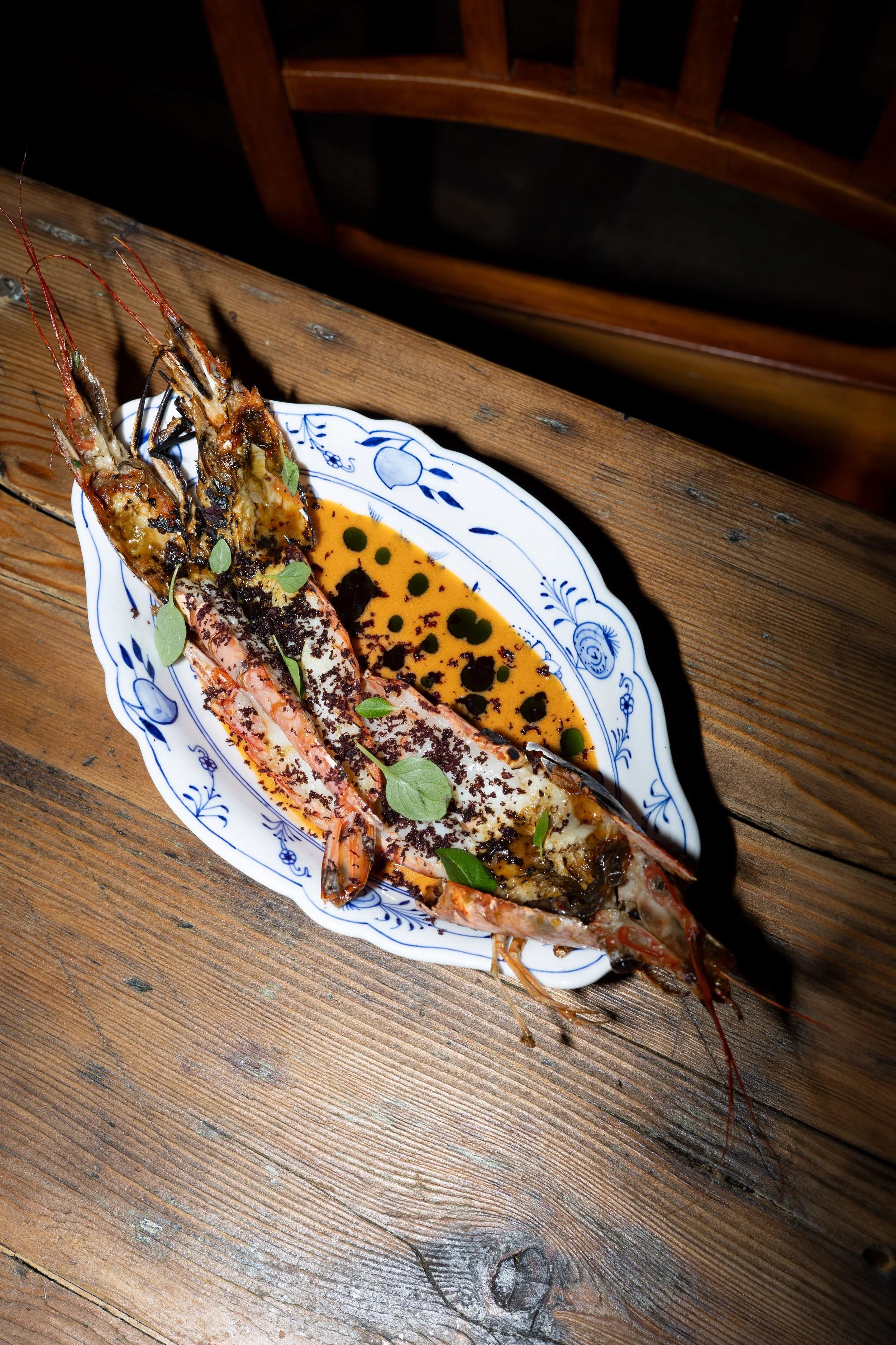 Grilled lobster tail on a decorative plate with herbs and sauce on a wooden table.