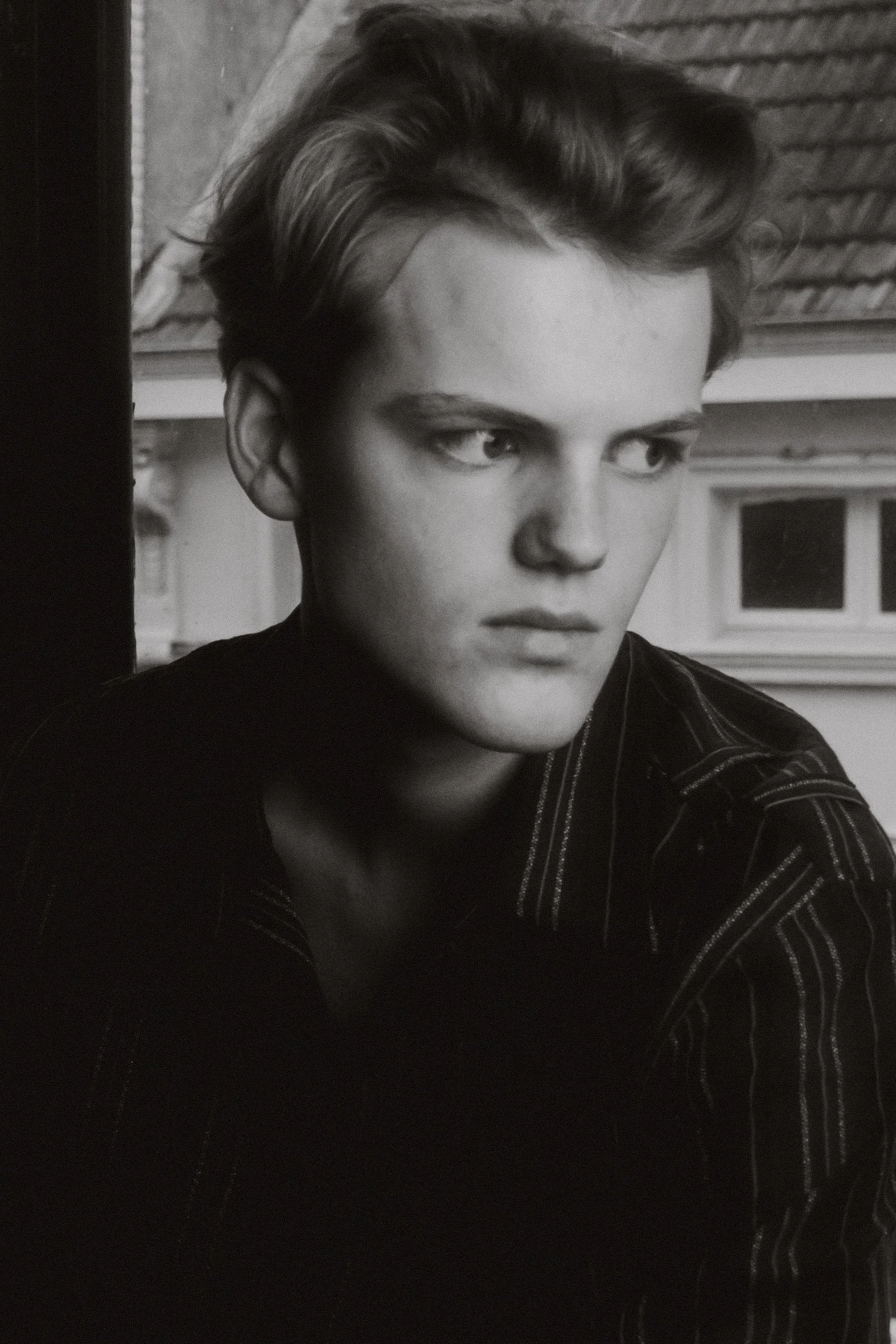 Black and white photo of a young man with styled hair, wearing a striped shirt, gazing thoughtfully to the side.