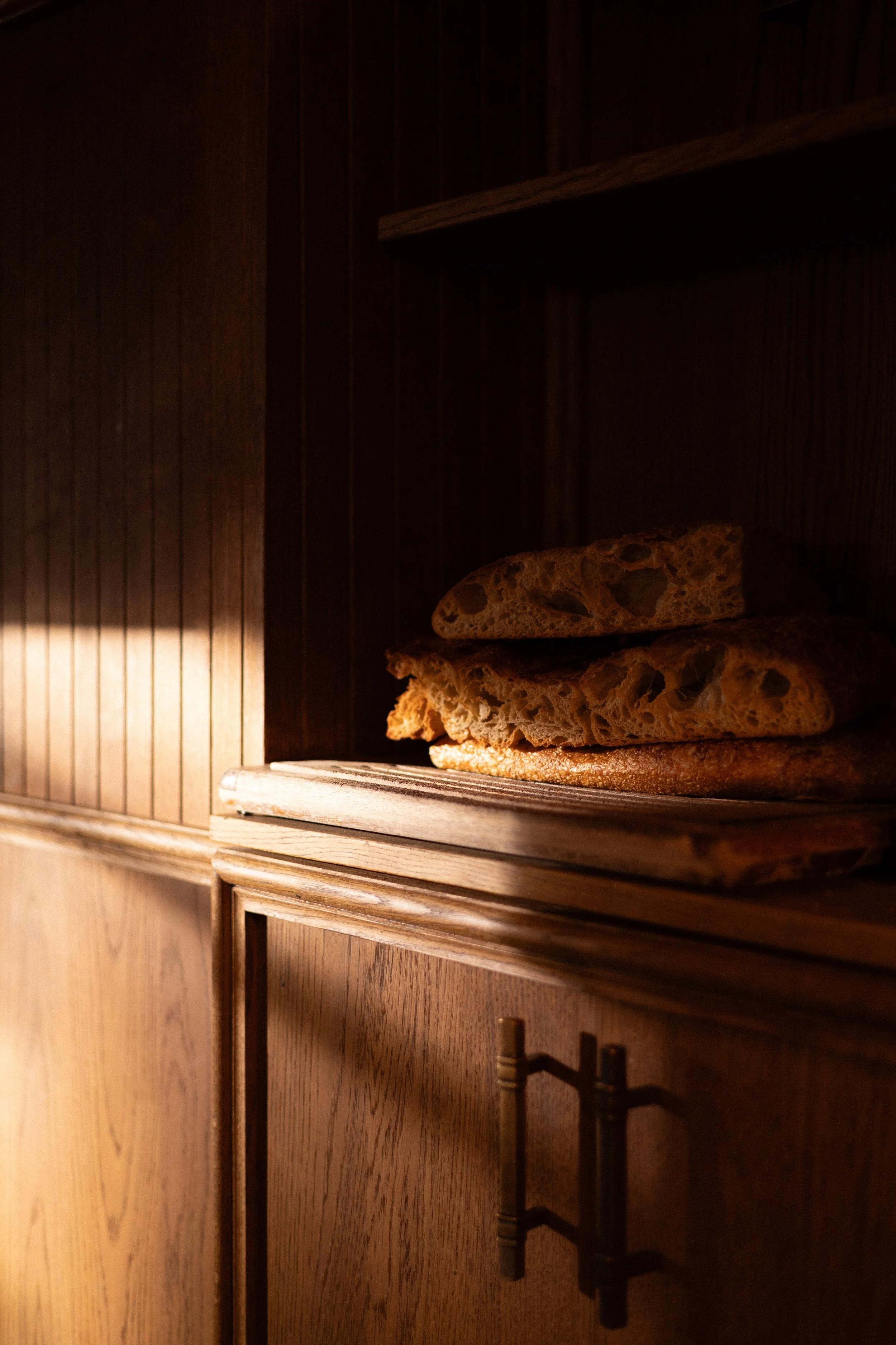 Stacked slices of focaccia bread on a wooden shelf inside a dark wooden cabinet.
