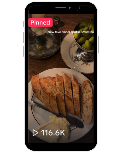 Plate of breaded fried food with a dollop of butter or cream, alongside a slice of multigrain bread, with a bowl of green olives and a container of salt in the background.