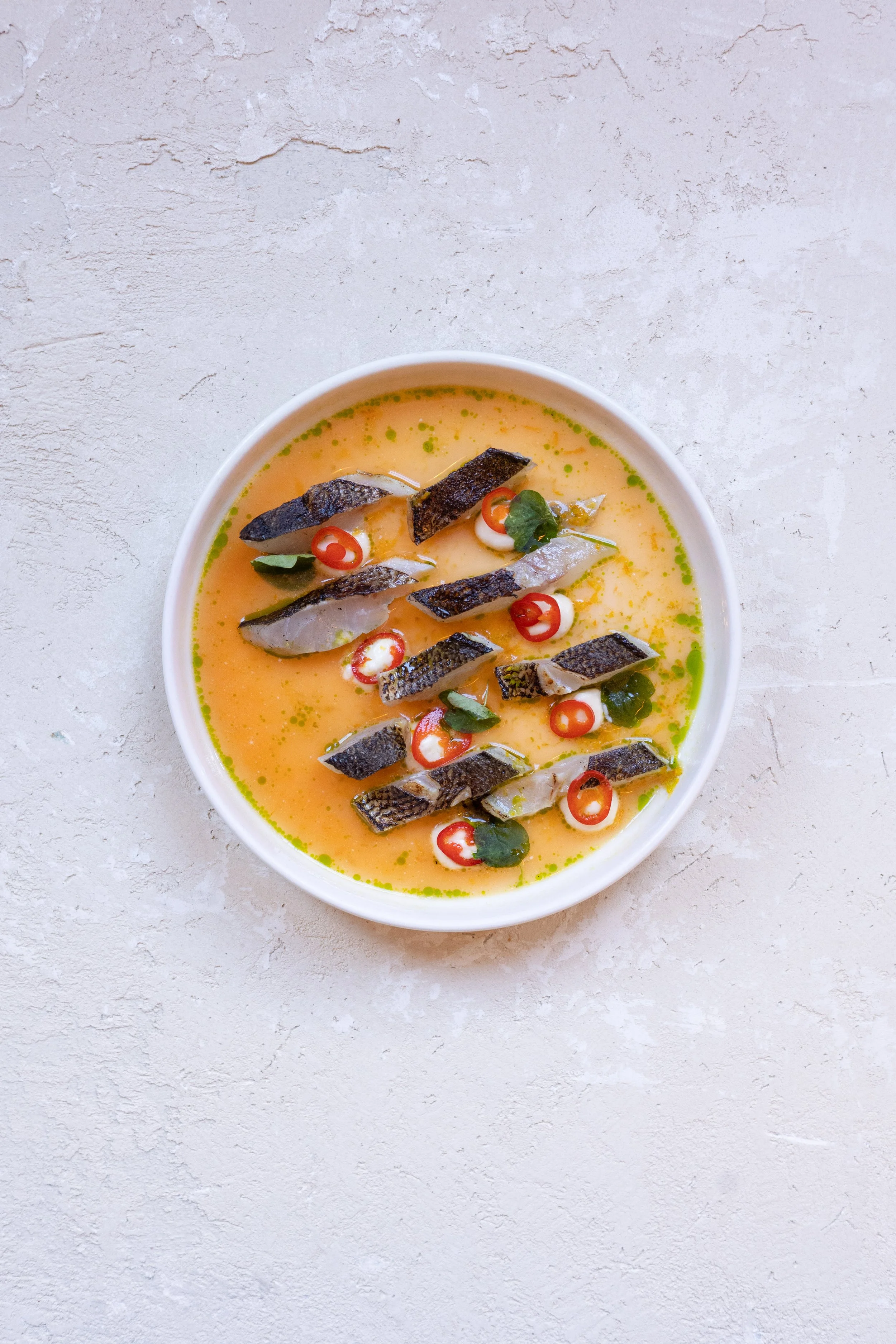 Bowl of fish ceviche topped with sliced chili peppers, cilantro, and fish pieces in a citrus-based marinade.