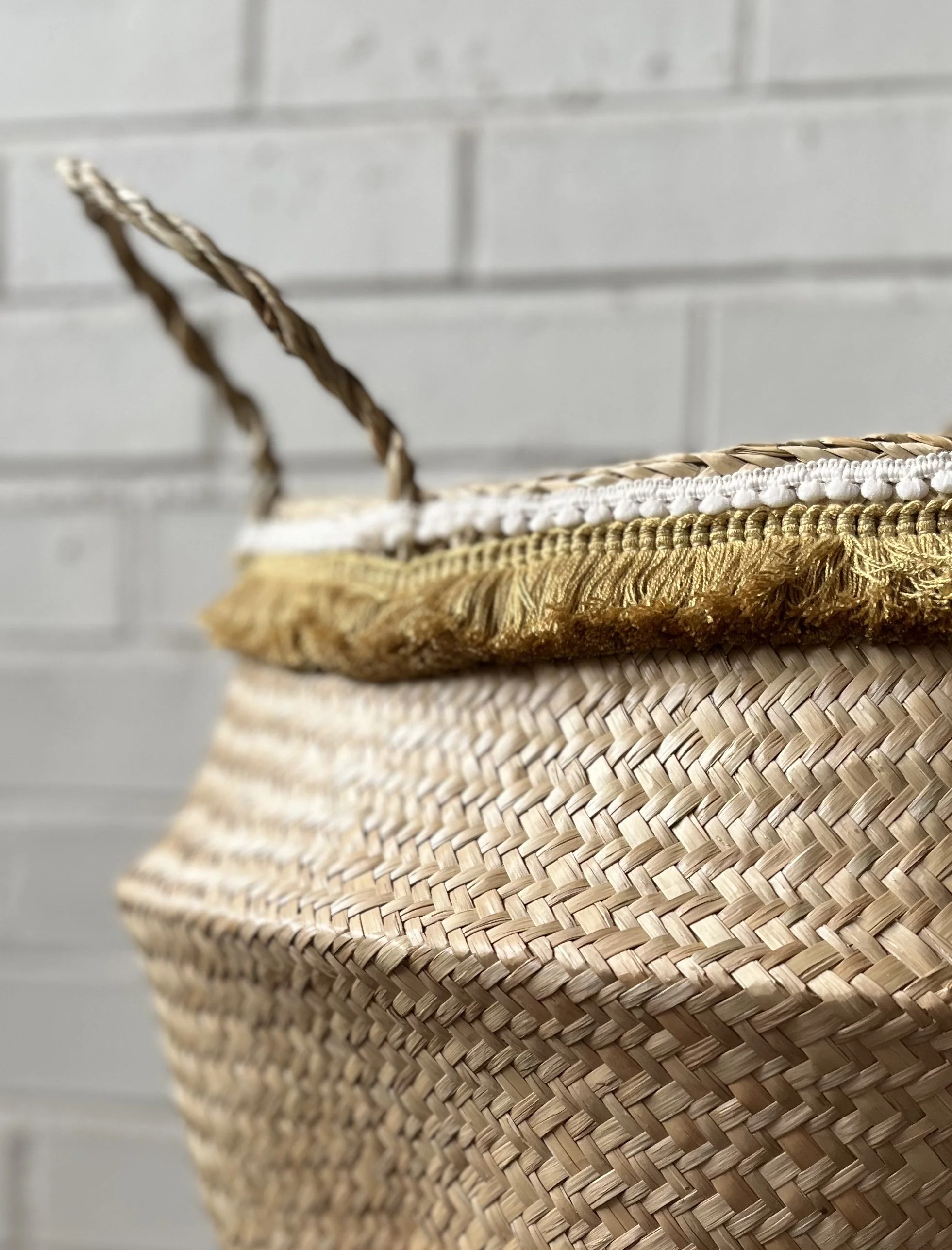 Close-up photo of a woven straw basket with a fabric trim, set against a white wall with horizontal lines.