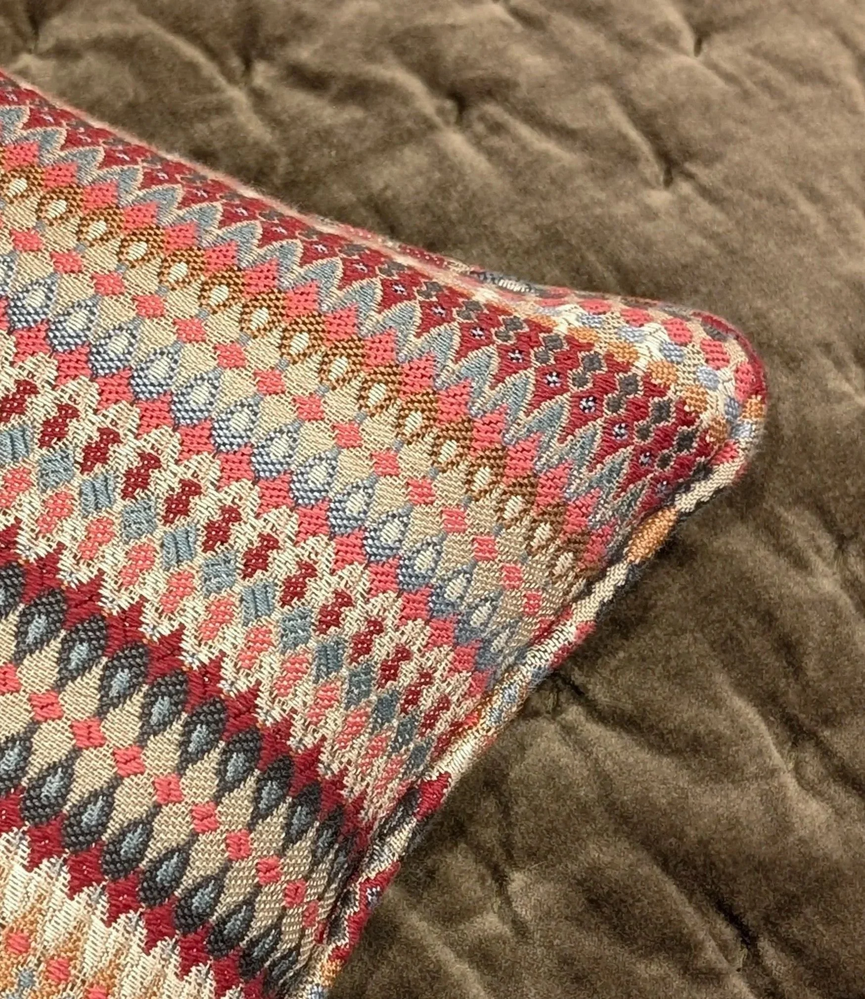 Close-up of a textured textile fabric featuring a colorful plaid pattern with red, pink, black, and cream colors, alongside a portion of a soft brown fabric.