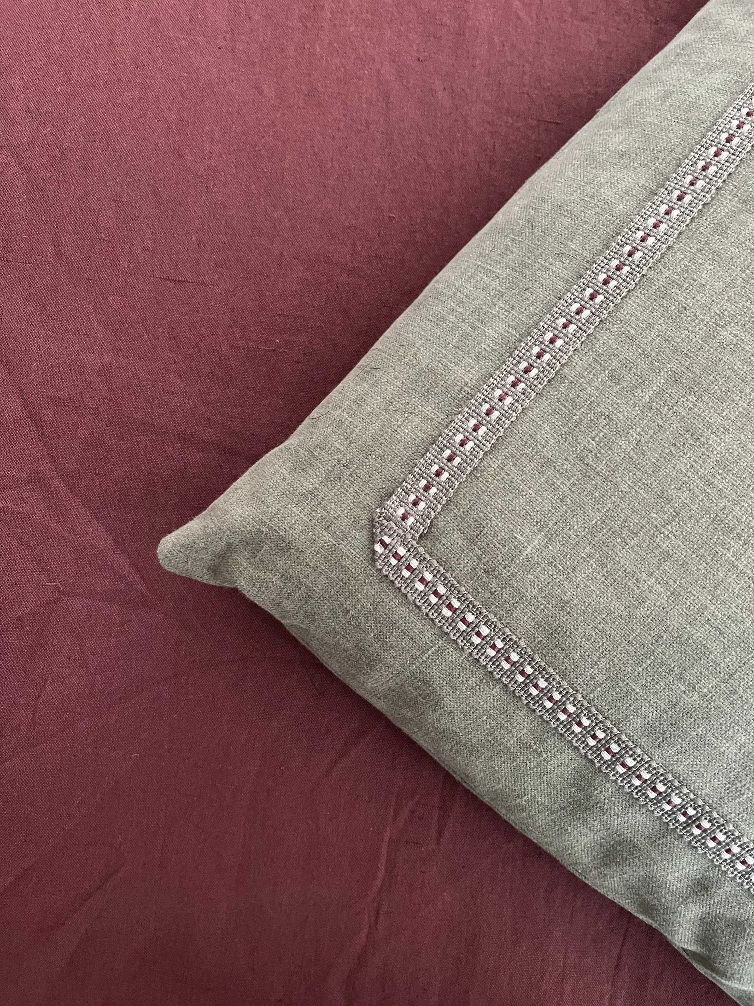 Close-up of a beige cushion with a decorative stitched border, resting on a red fabric surface.