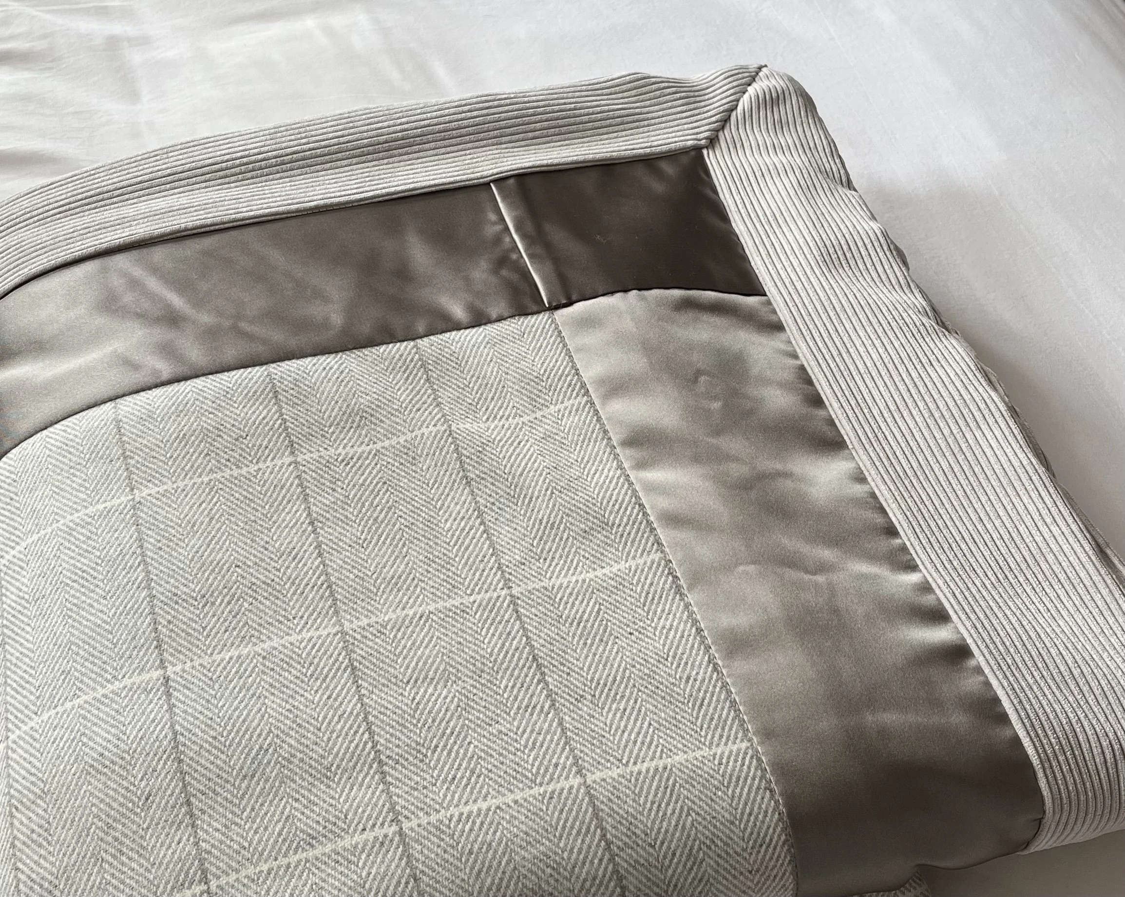 Close-up of a folded fabric item with a gray ribbed elastic waistband, beige fabric with a quilted pattern, and shiny satin-like material in the middle, resting on a white surface.
