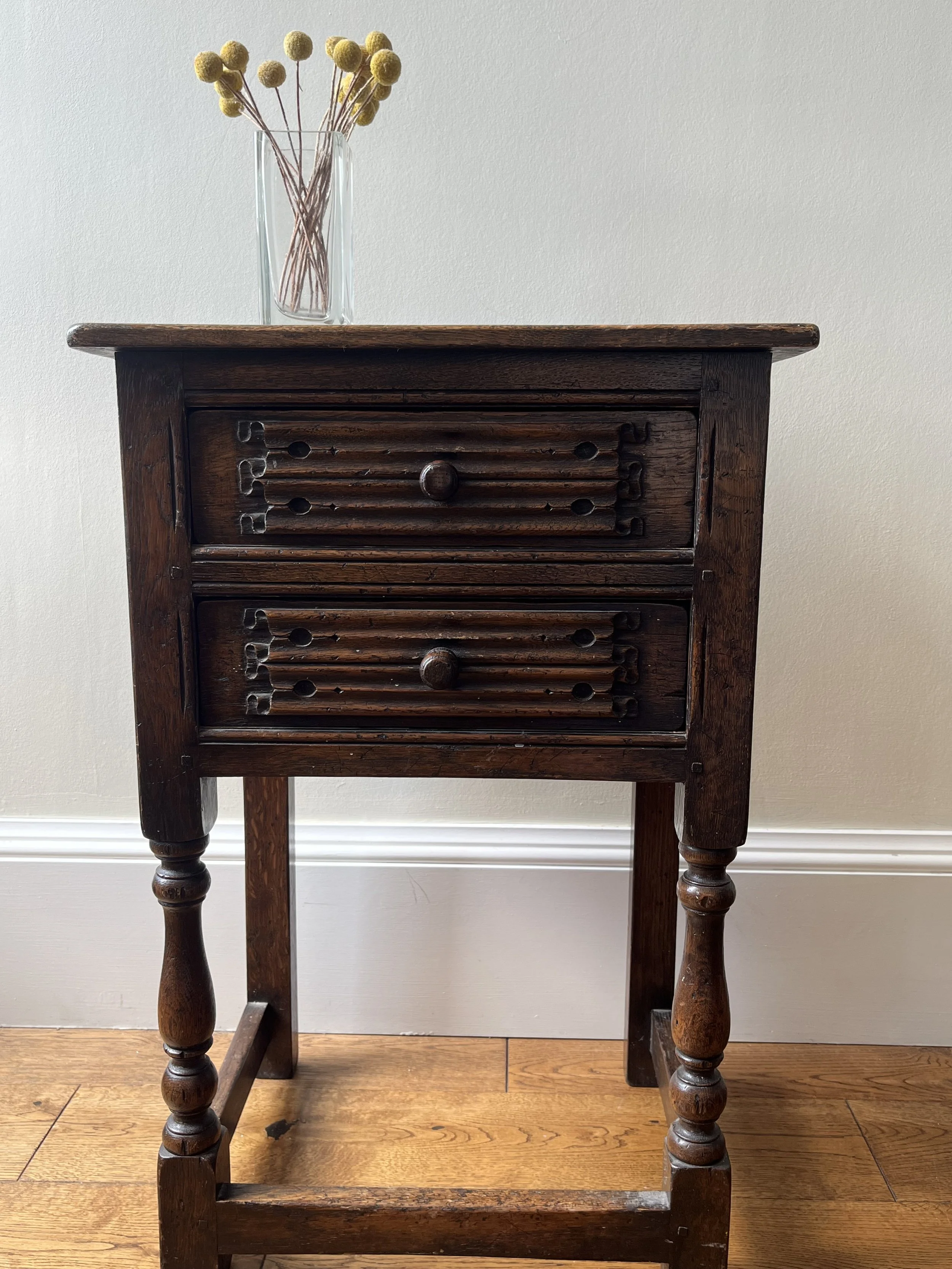 A small antique wooden cabinet with multiple small drawers, standing on four turned legs, with a glass vase containing yellow Billy ball flowers placed on top.