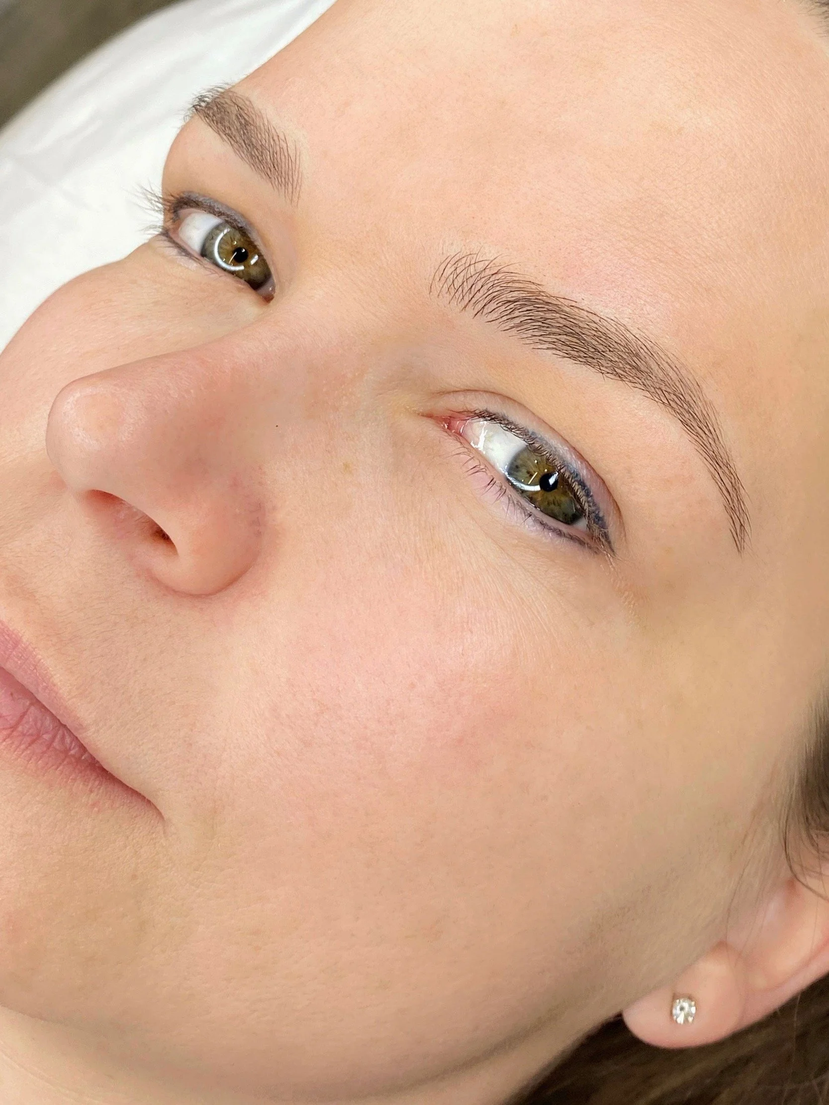 Close-up of a woman's face with focus on her brown eyes, groomed eyebrows, and smooth skin.