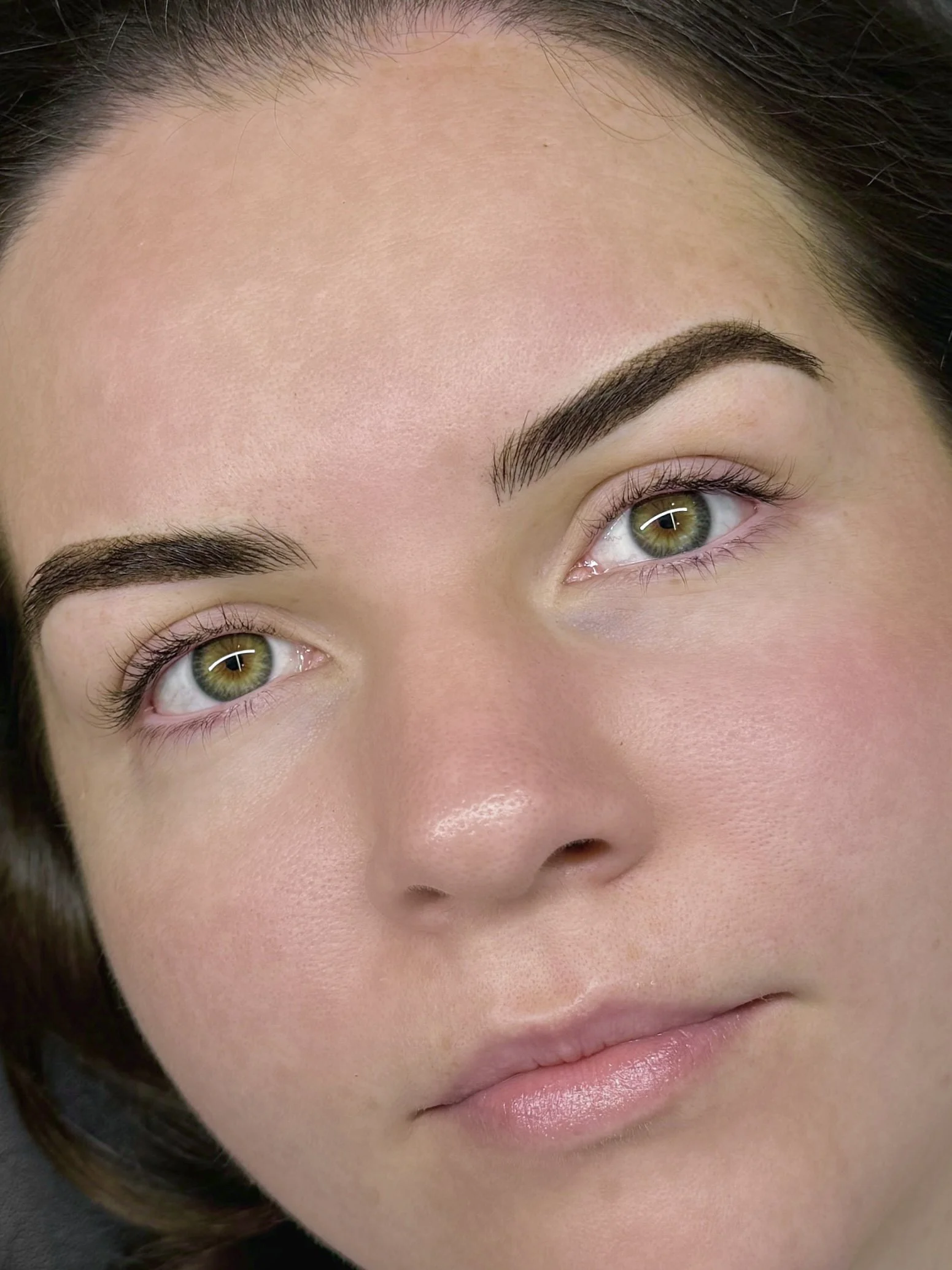 Close-up of a woman's face showing clear skin, well-groomed eyebrows, and green eyes.