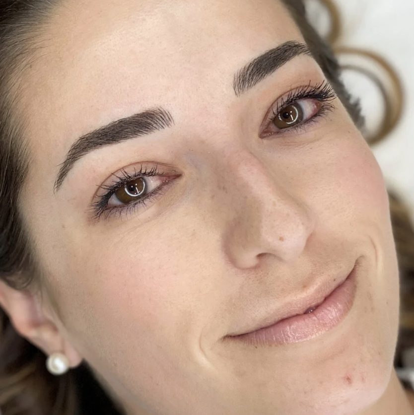 Close-up of a woman's face showing her well-groomed eyebrows, brown eyes, and a slight smile, with pearl earrings visible.