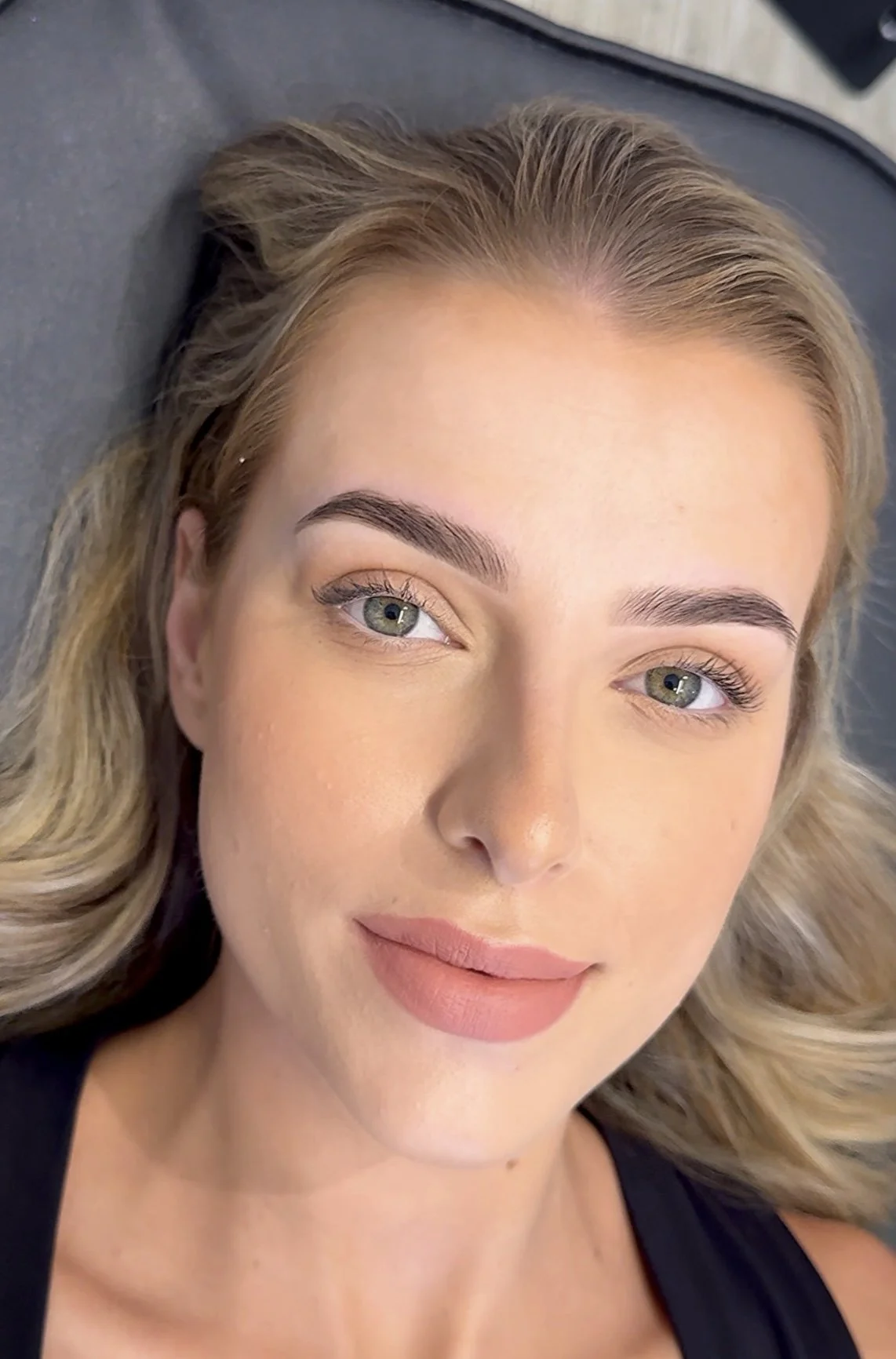 A woman with blonde hair and blue eyes lying on a surface, looking at the camera, with a slight smile.